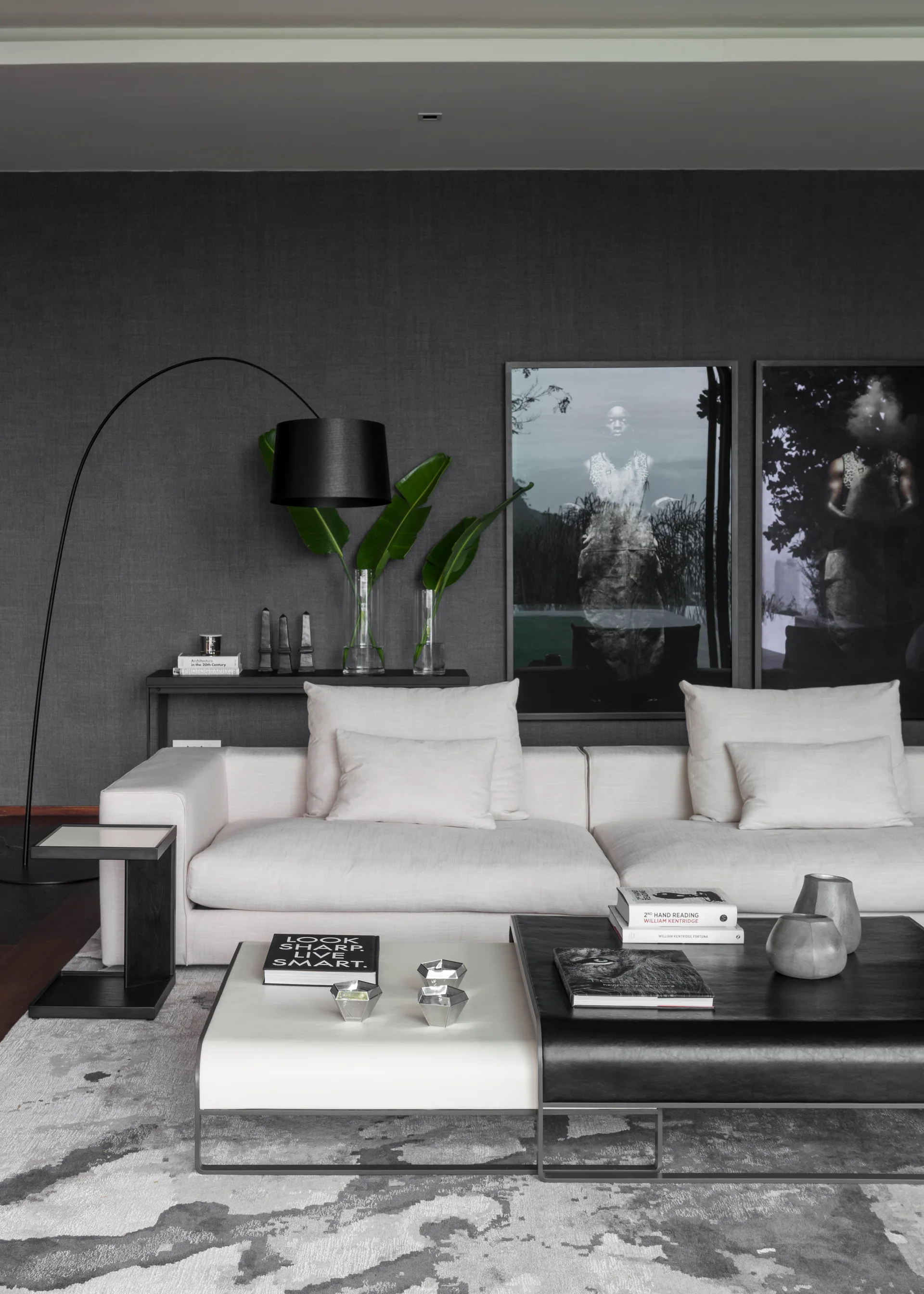 A modern living room features a cream-colored sofa set against a dark grey textured wall with a black arc floor lamp and a tiered coffee table.