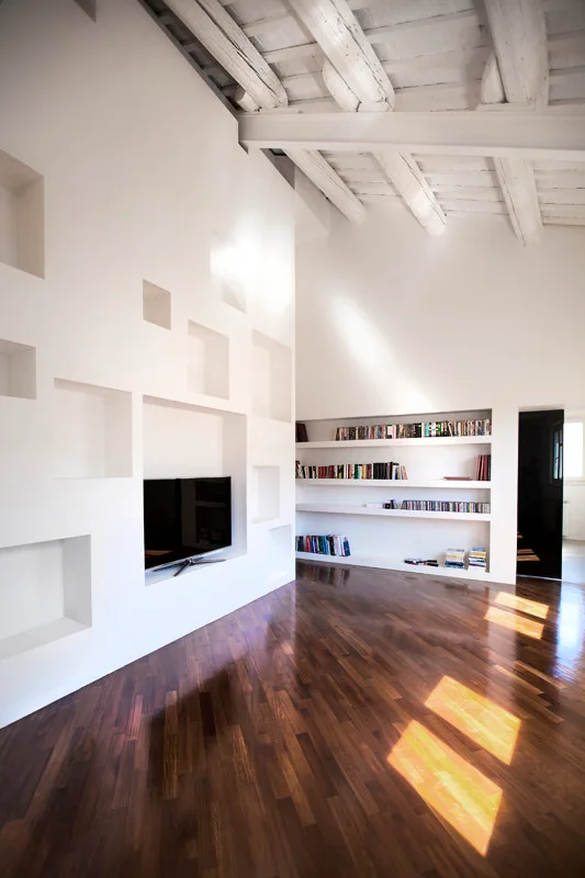 A minimalist living room features white walls with custom square recessed niches, a sloped ceiling with exposed white beams, and glossy dark wood floors.