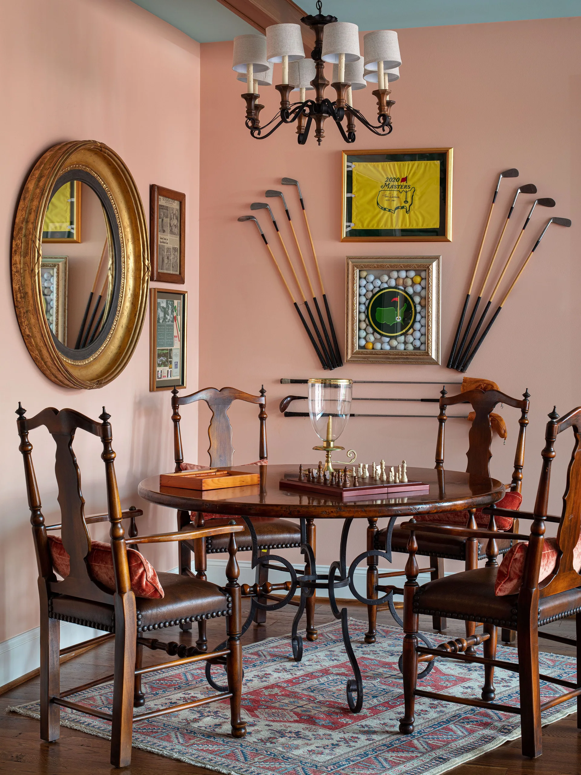 A dark wood game table with a chess set sits on a patterned rug against peach walls decorated with golf memorabilia.