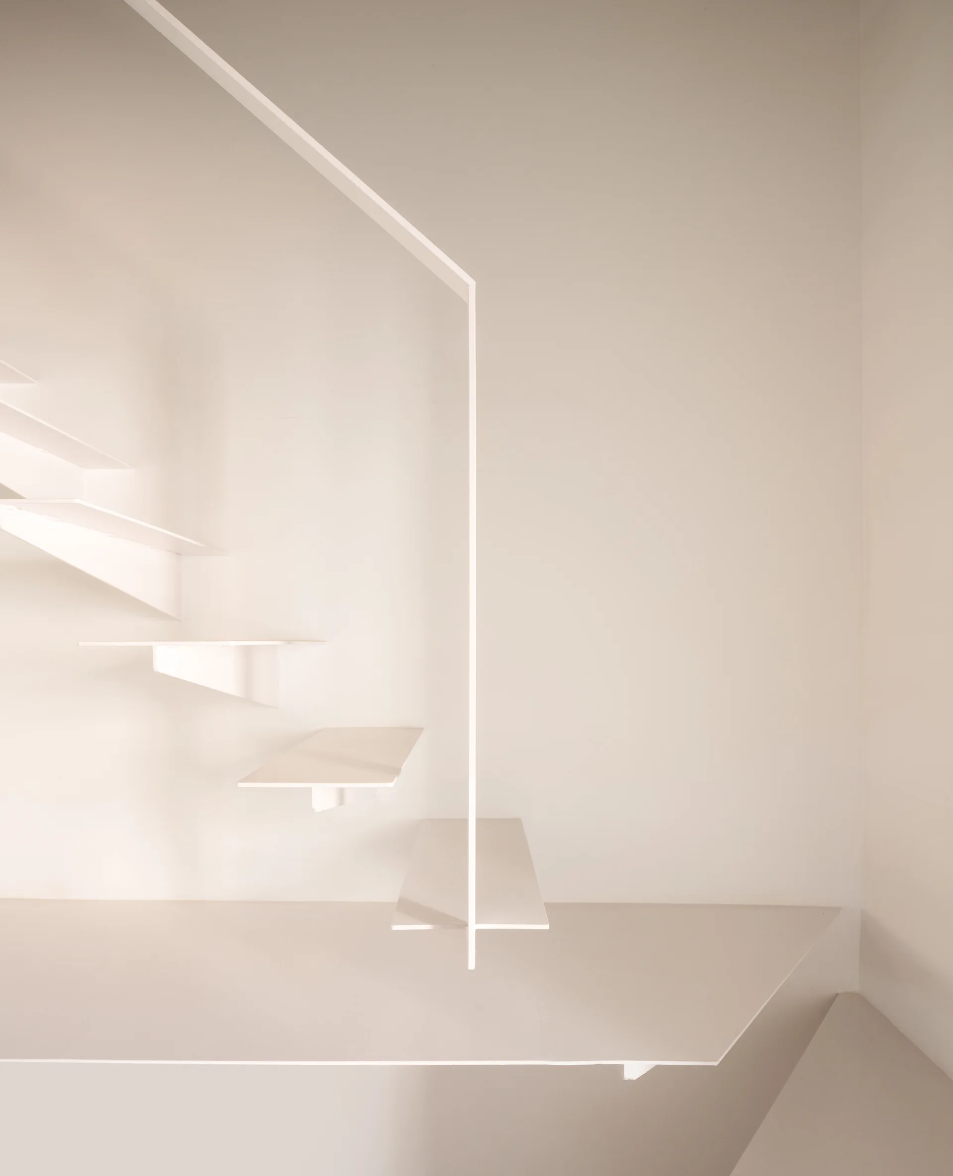A minimalist white staircase with cantilevered floating treads and a thin vertical support structure against a plain white wall.