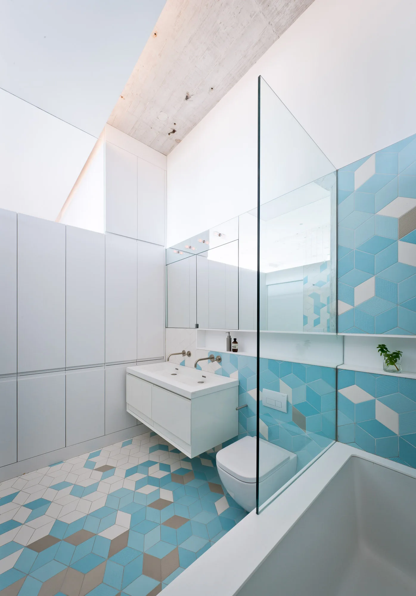 A modern bathroom with blue and white geometric tiles on the floor and walls, a wall-mounted white vanity, and tall minimalist storage cabinets.