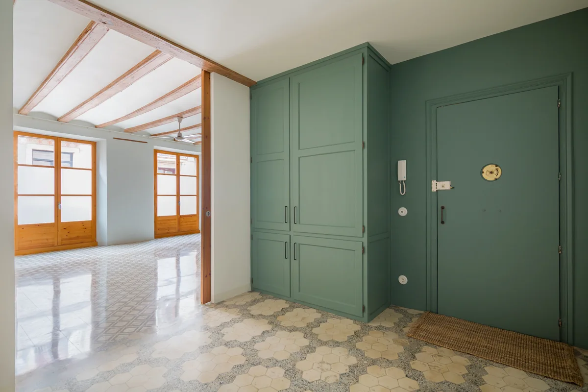 A sage green entryway featuring matching built-in cabinets and a front door next to patterned hexagonal tile flooring.