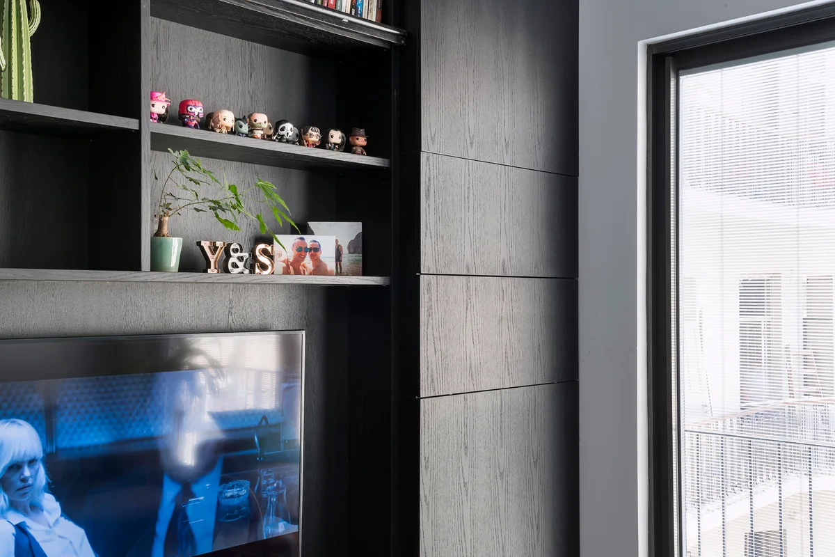 A close-up of a black wood-grain built-in media cabinet featuring open shelves with decor items next to a bright window.