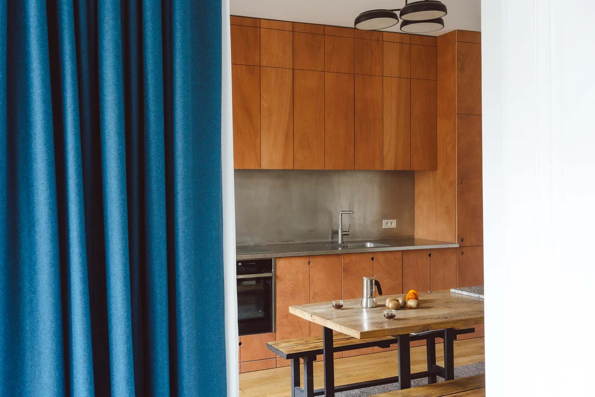 A modern kitchen features warm wood-toned cabinets, a metallic backsplash, and a rustic wooden dining table with bench seating.