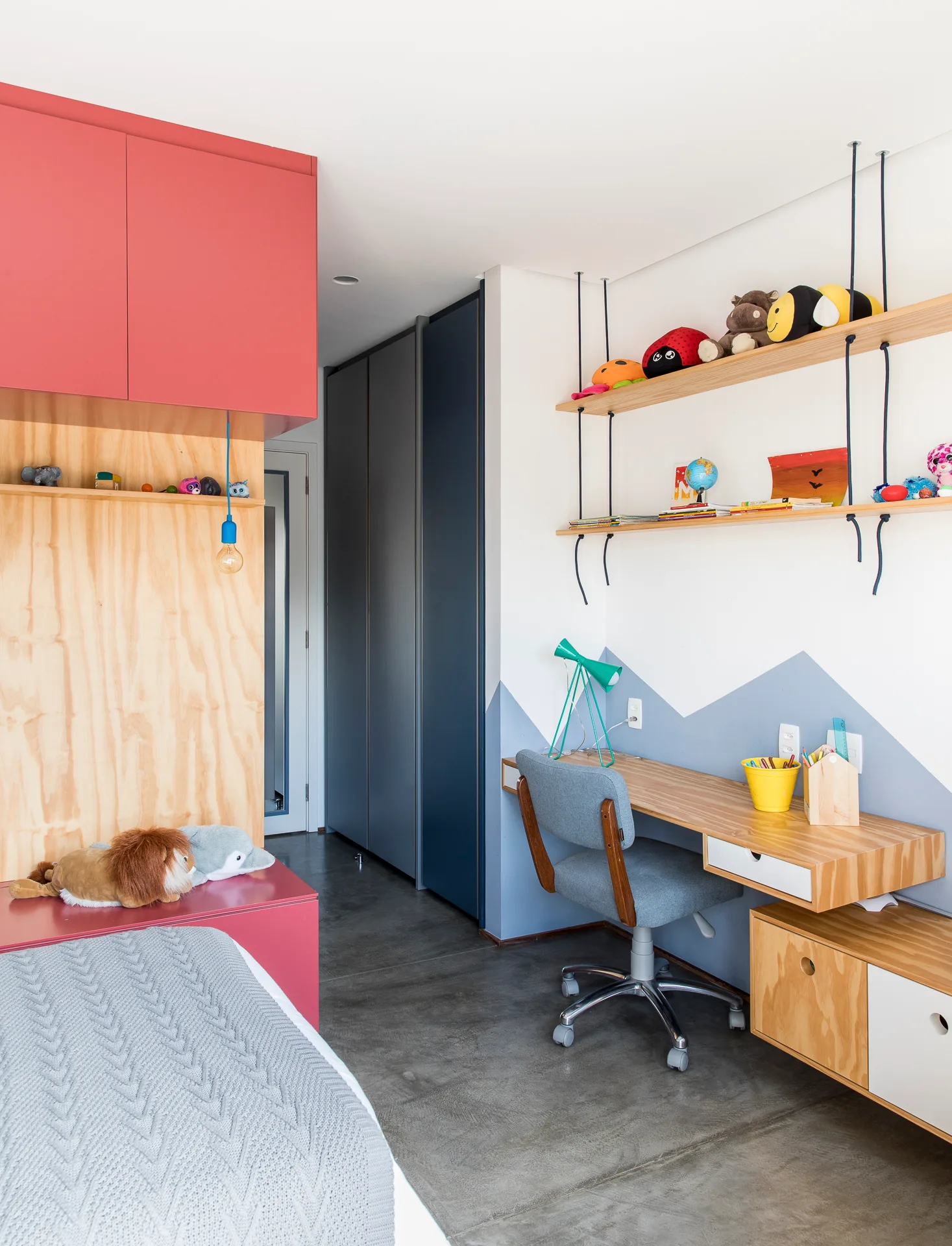 A children's bedroom features a floating wooden desk with a grey task chair, a geometric mountain mural wall, and open wooden hanging shelves.