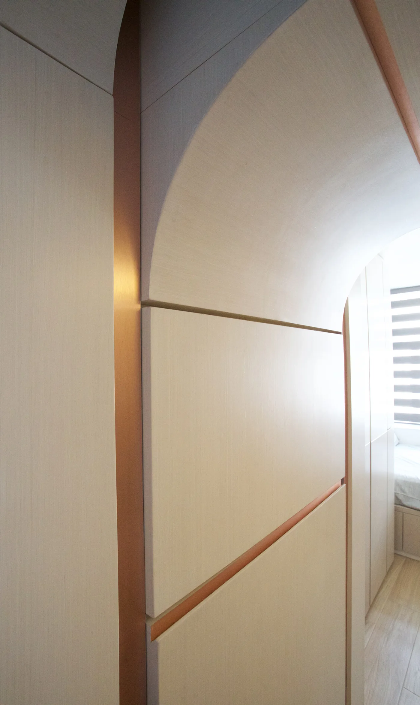 An interior view of a curved light beige wood partition wall accented by thin copper metallic vertical and horizontal inlays.