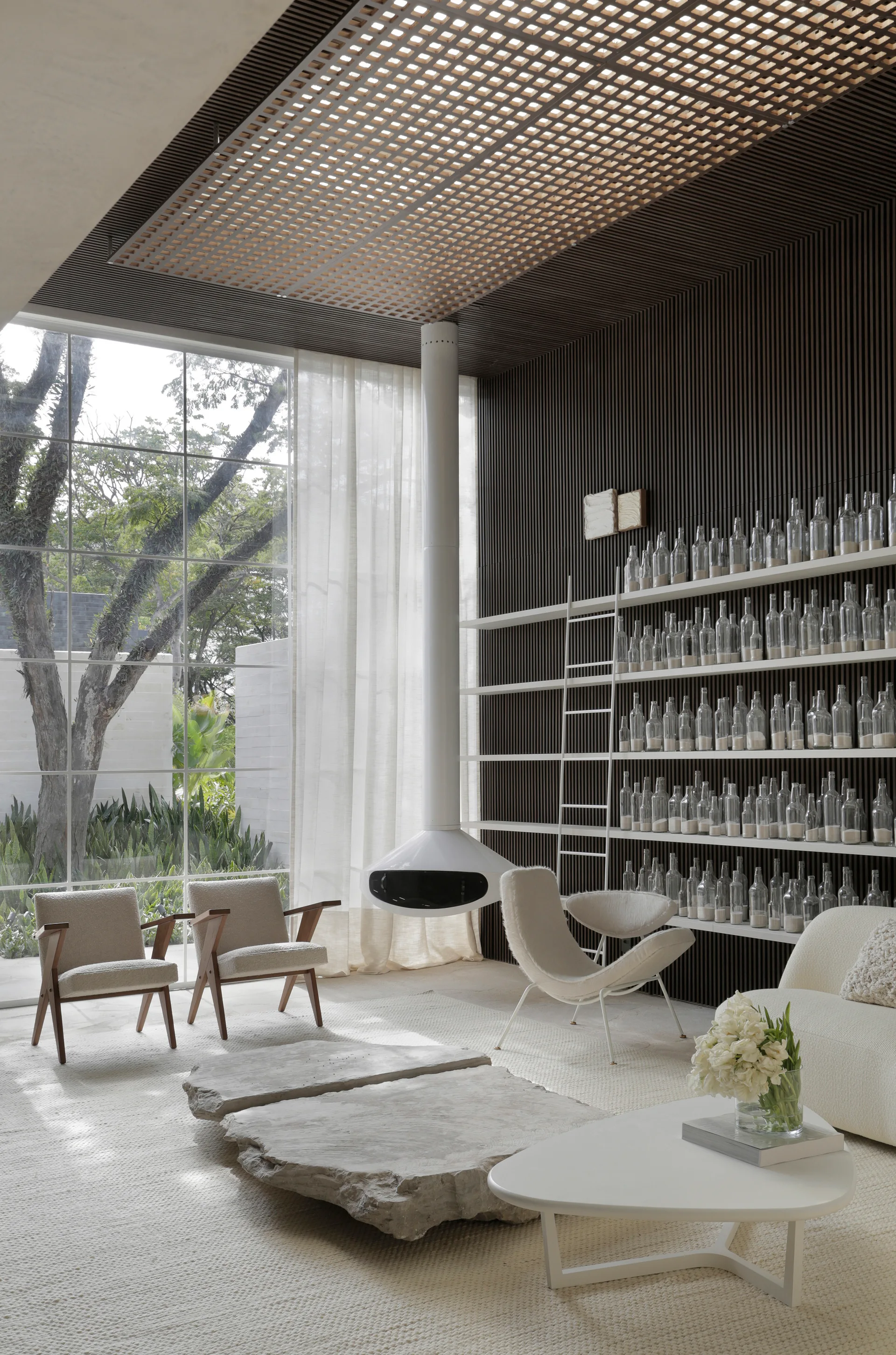 A contemporary living room featuring a suspended white fireplace, dark slatted walls, and organic stone slab coffee tables.