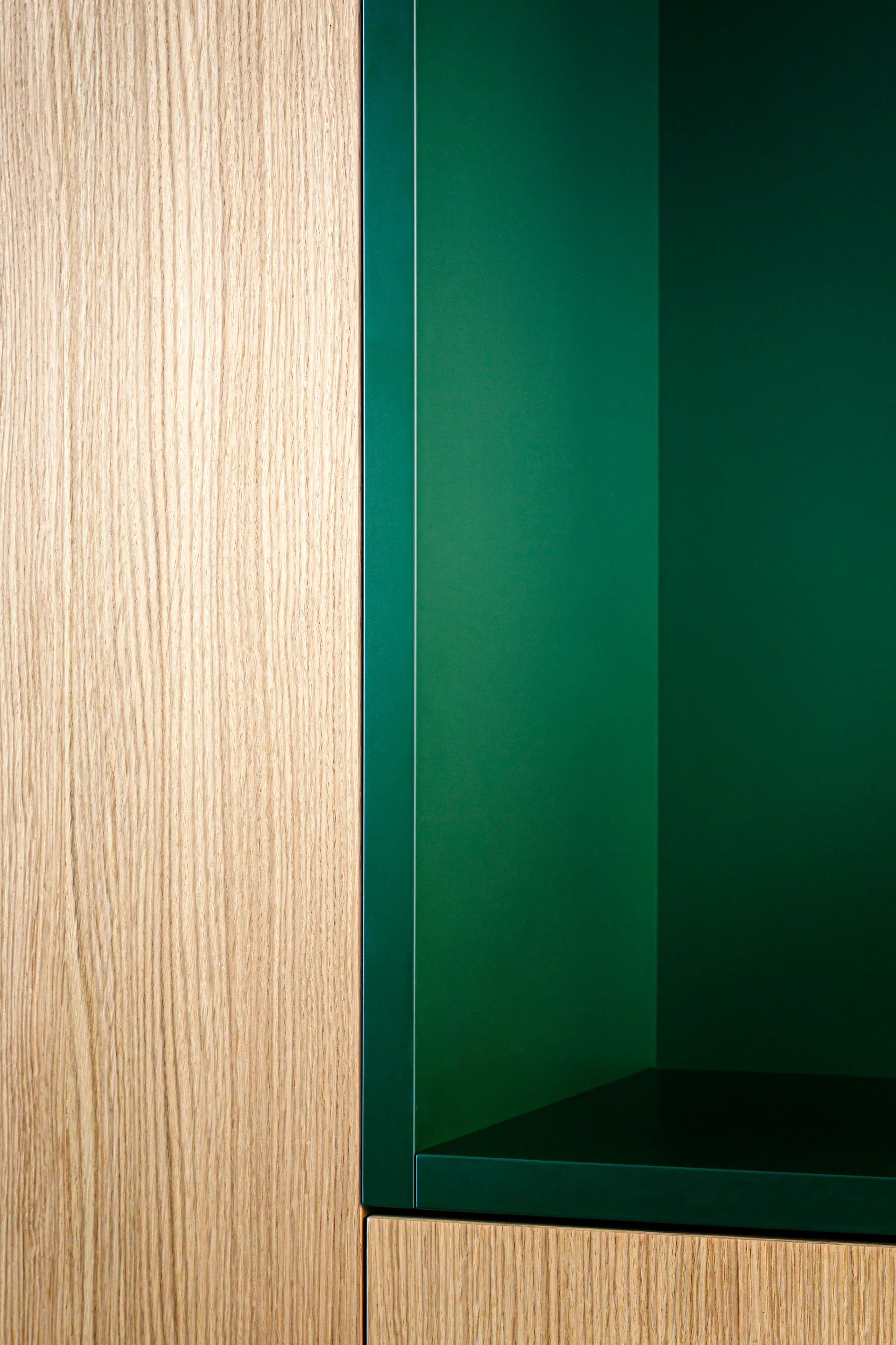 A close-up of custom cabinetry showing vertical light oak wood grain panels next to a matte forest green recessed shelf.