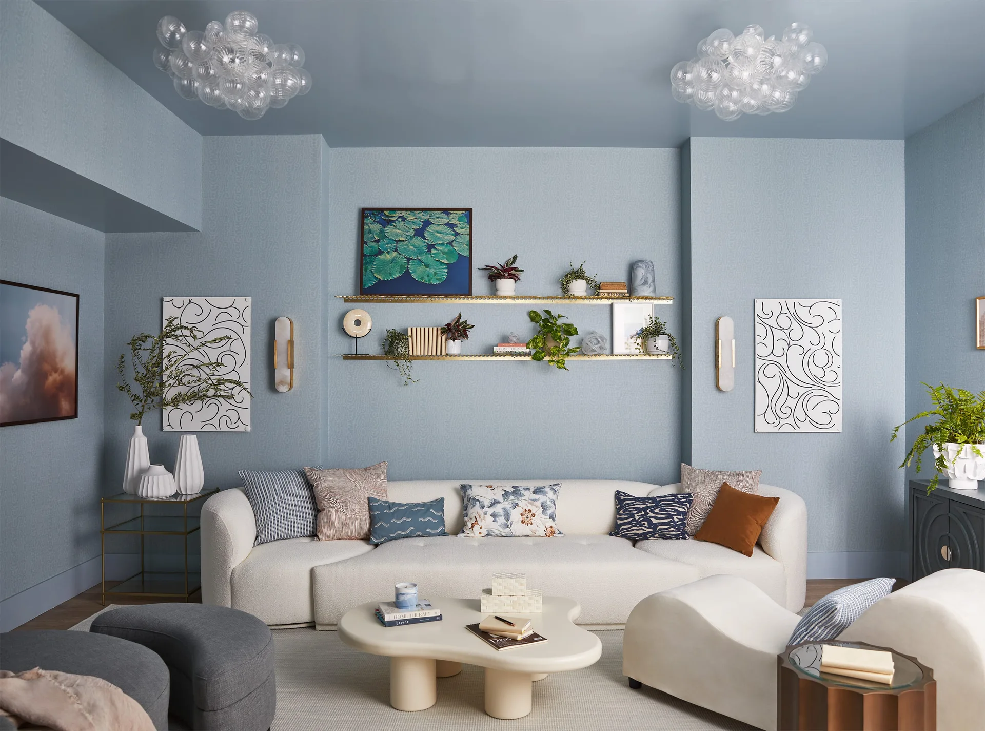 A contemporary living room featuring light blue textured walls, a matching blue ceiling, a cream curved sofa, and gold wall shelving.