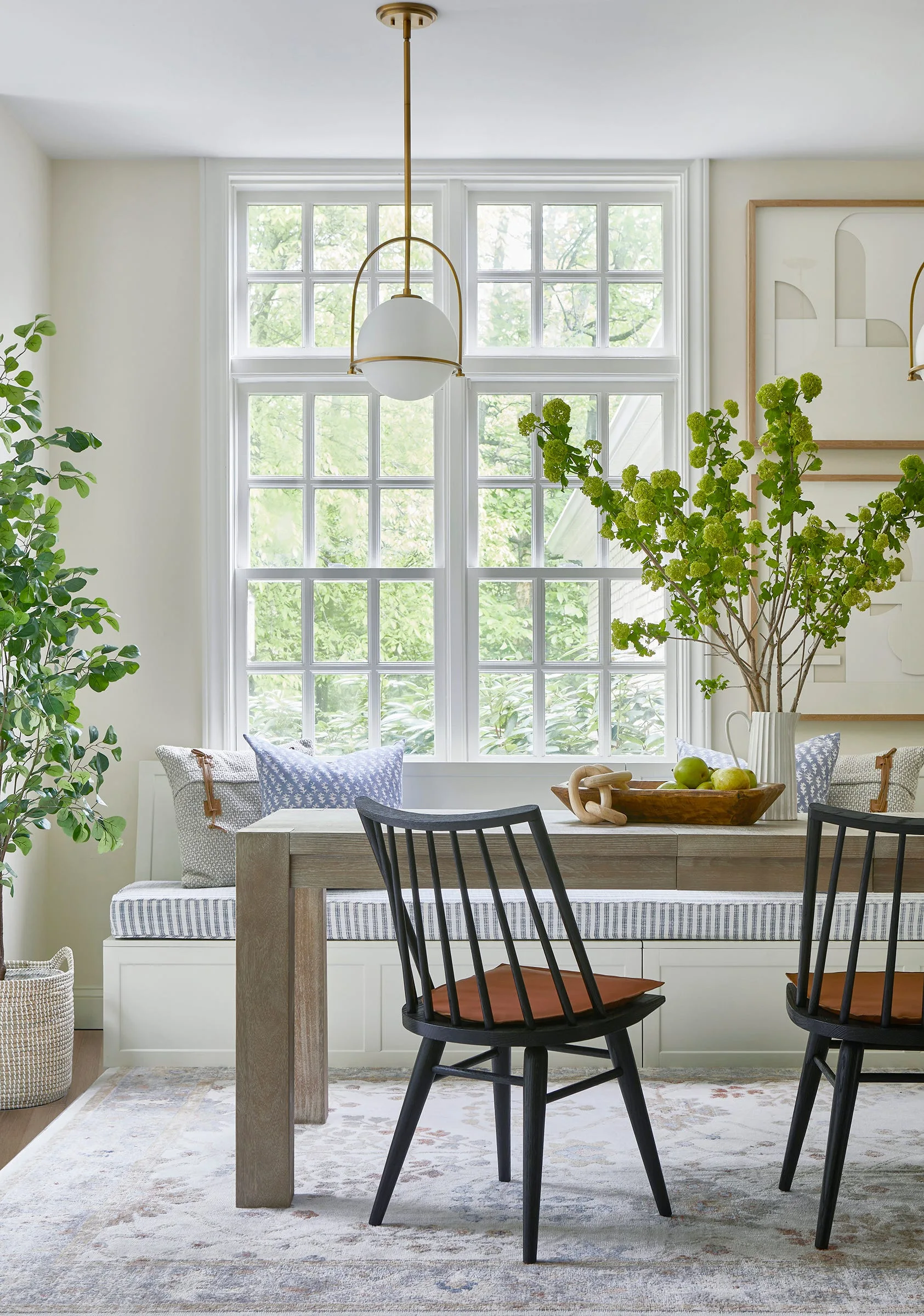 A bright dining nook features a wood table, black spindle chairs, and a built-in bench under a large multi-pane window.