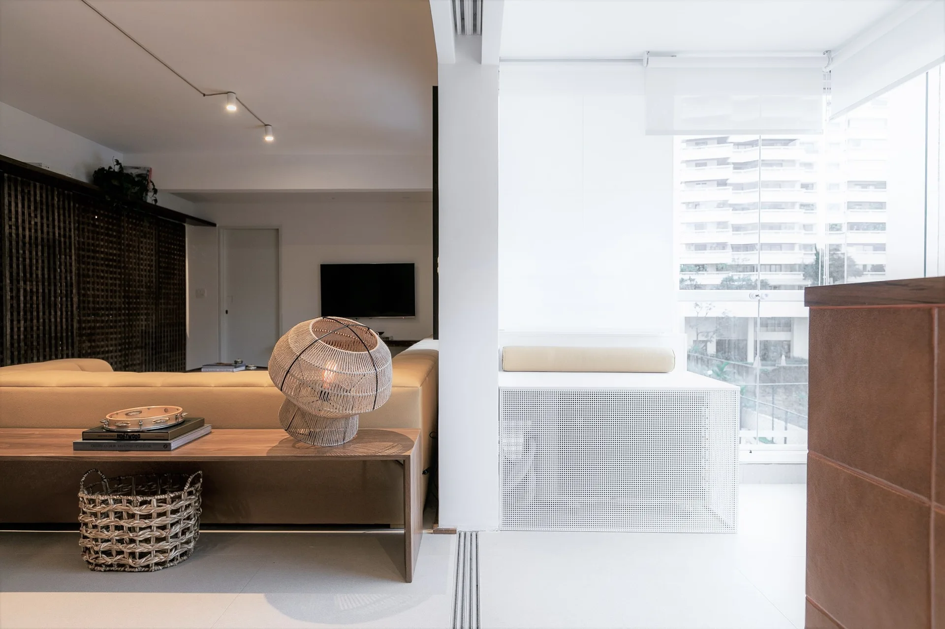 A minimalist living room features a tan sofa with a low wooden console table behind it holding a woven sculptural table lamp.