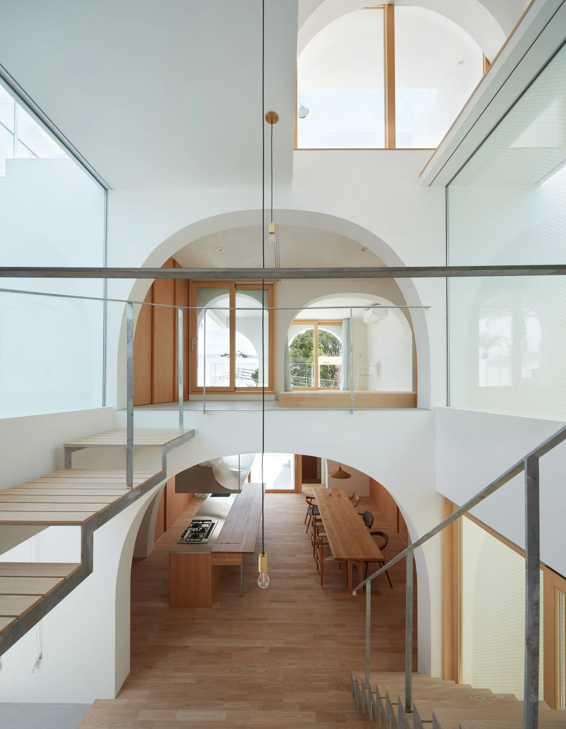 A multi-level minimalist interior featuring stacked white archways, light wood floors, floating stairs, and a kitchen below.