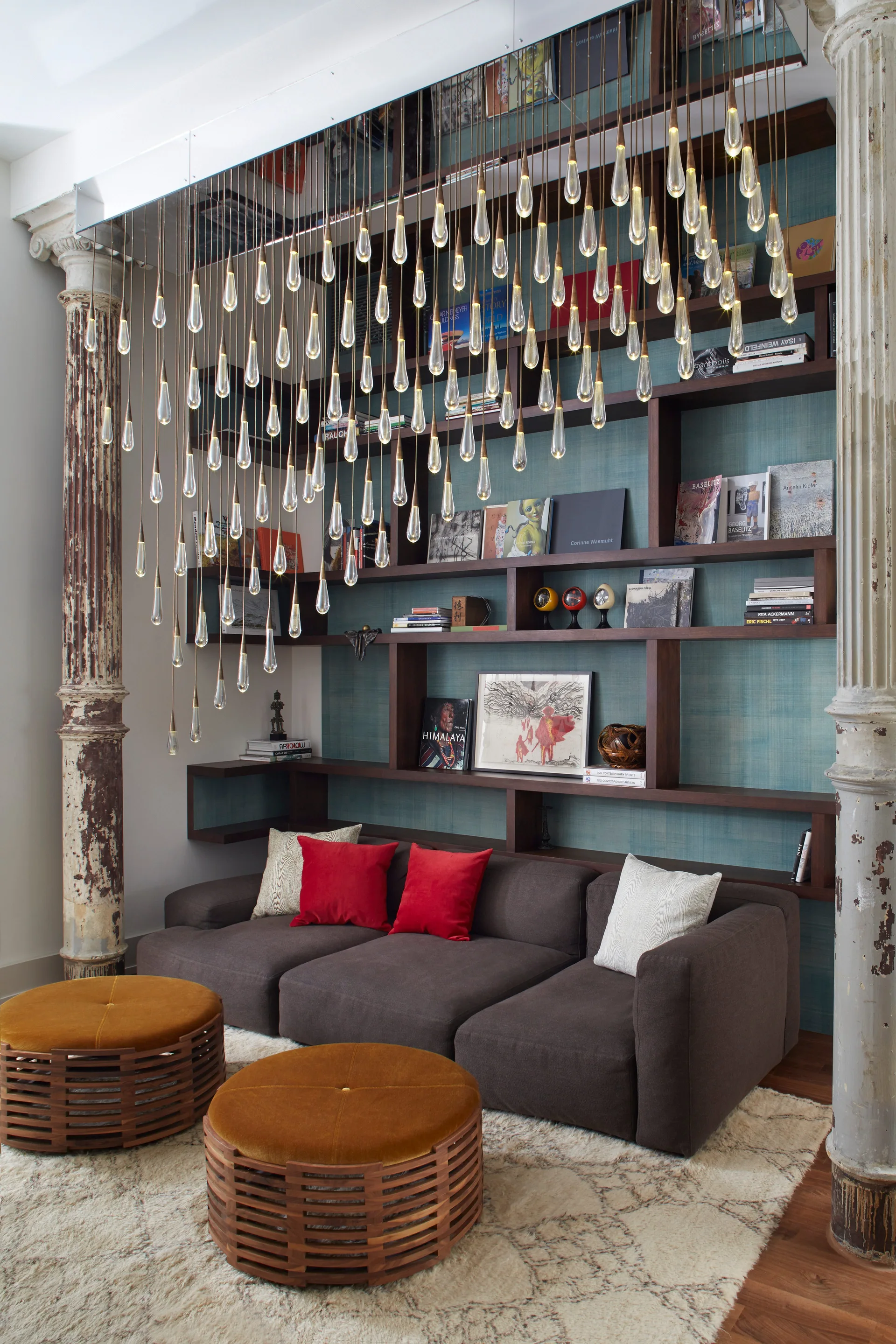 A dark sofa sits before teal-backed shelves flanked by distressed columns under a hanging cascade of glass teardrop lights.