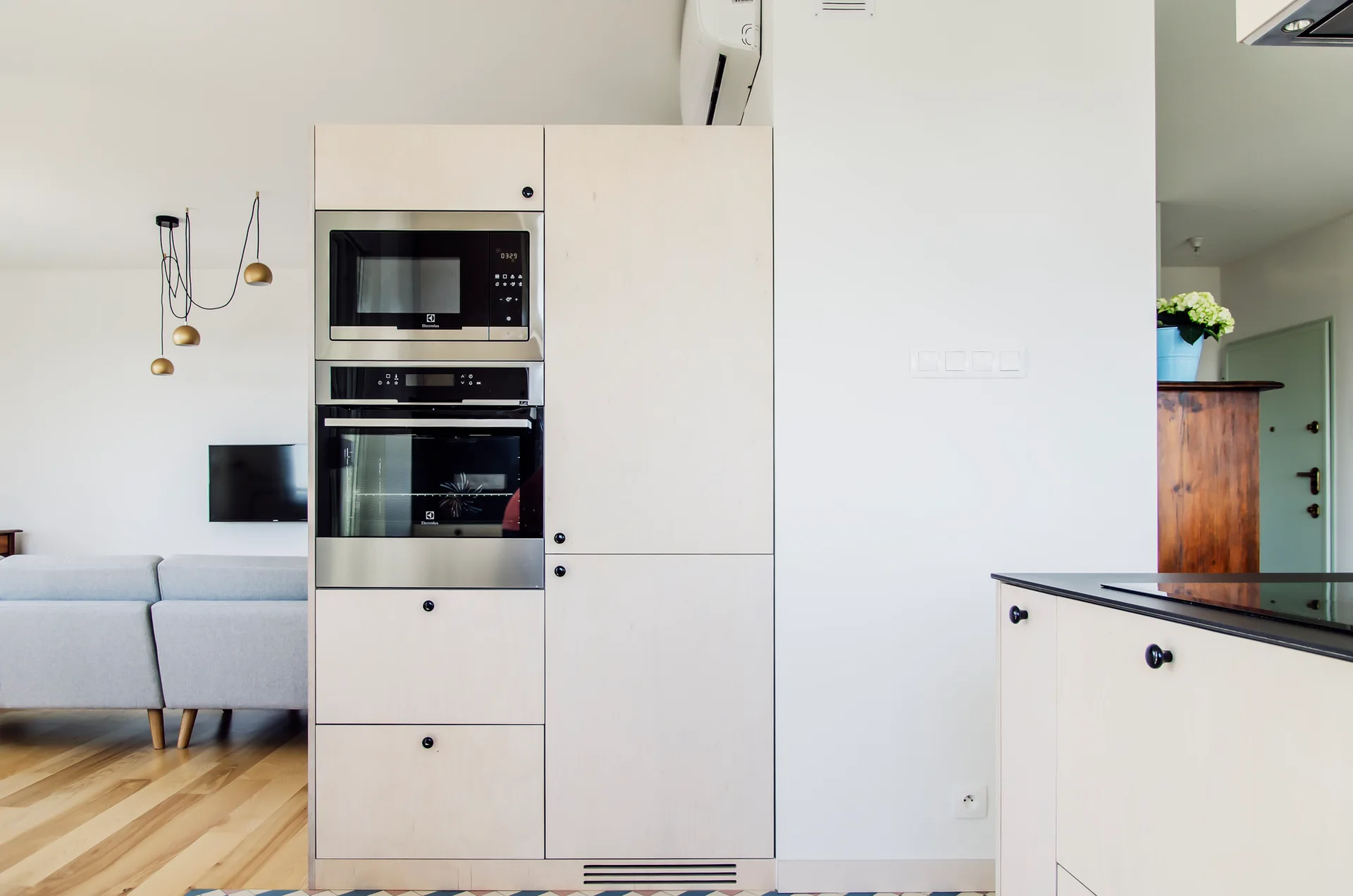 Built-in light wood kitchen cabinets with integrated appliances stand next to a white wall in an open-plan apartment.