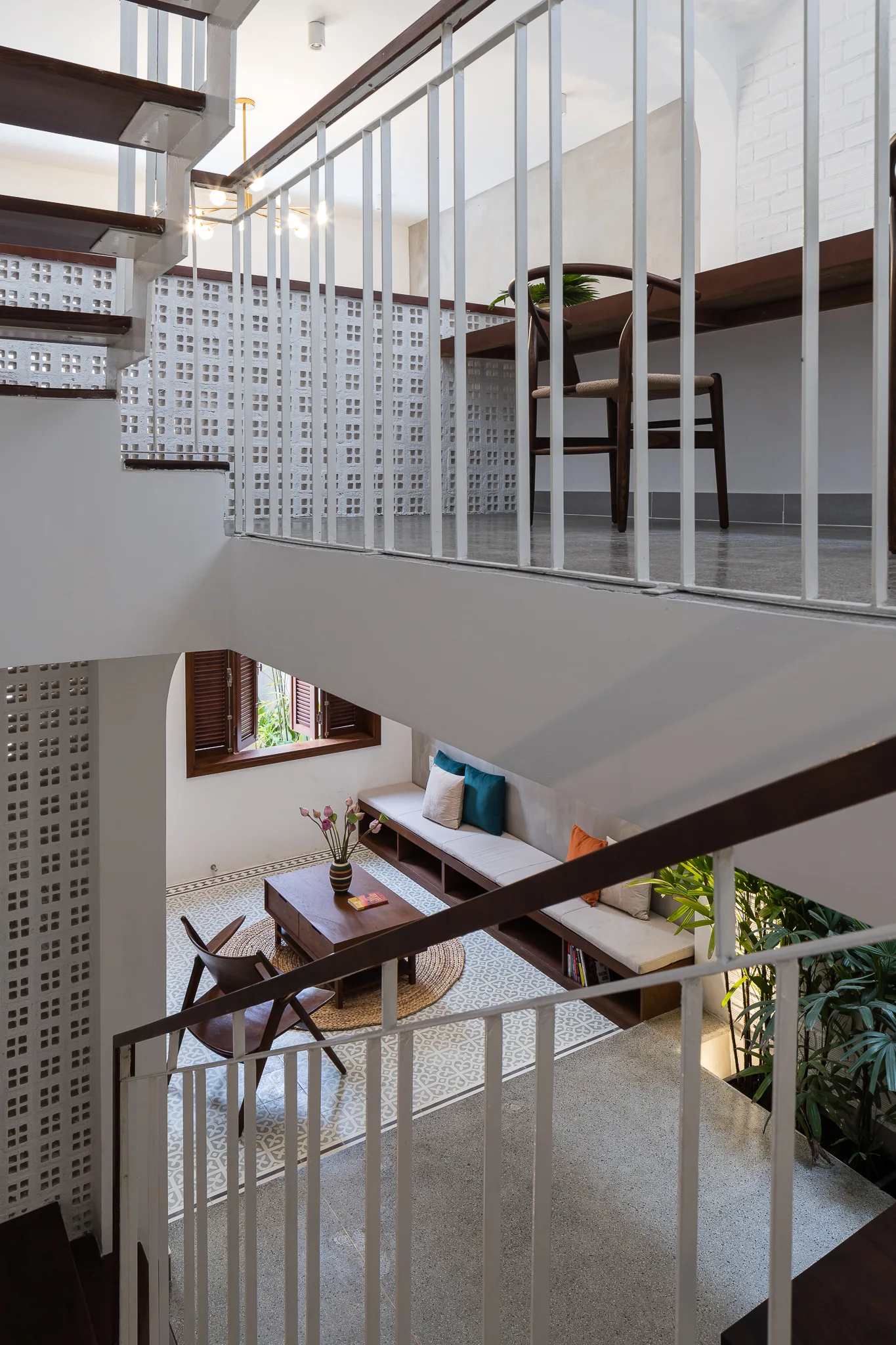 An overhead view of a home's staircase looking down onto a living area with patterned floor tiles, a built-in wooden bench, and white breeze block walls.