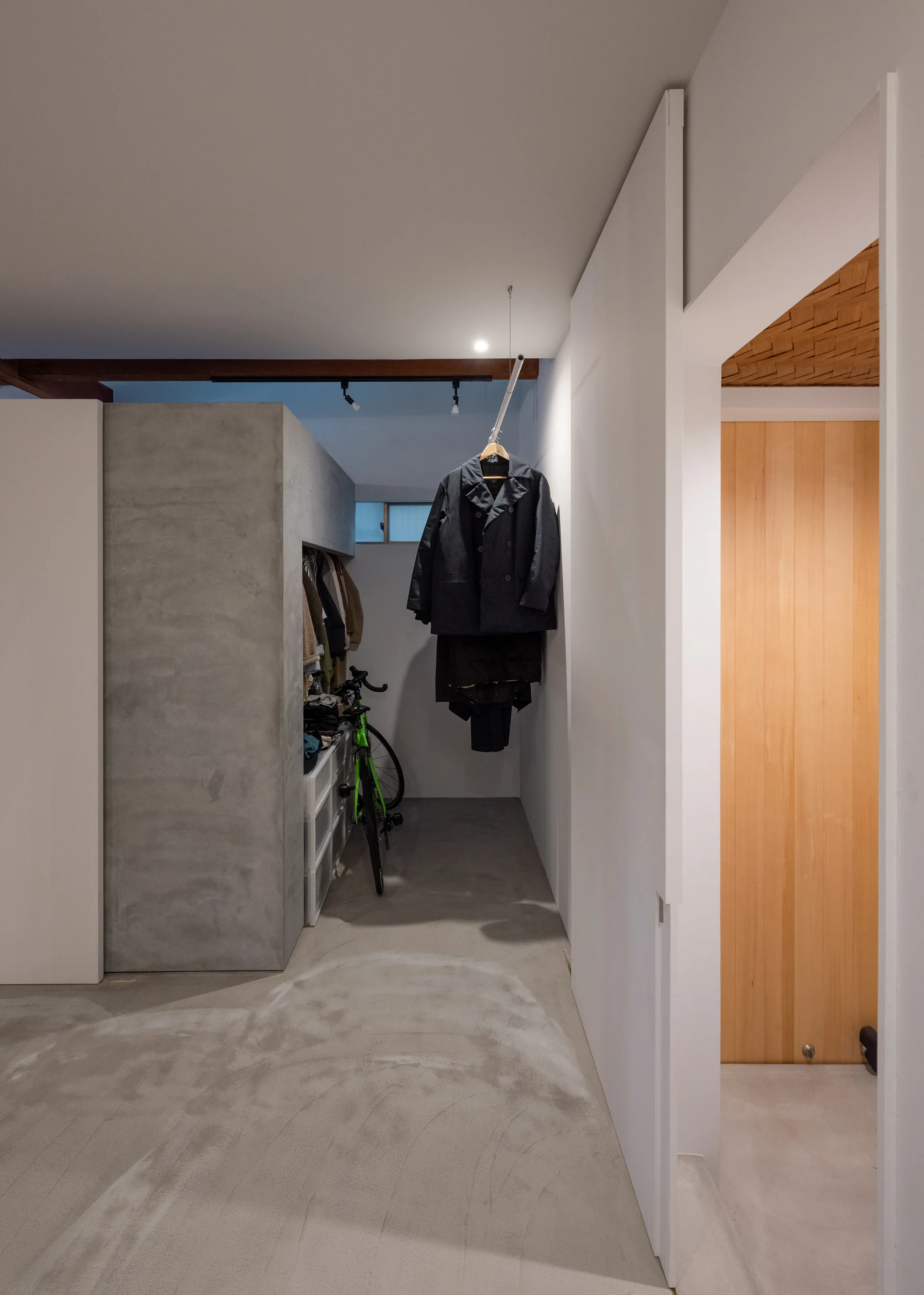 A minimalist walk-in closet featuring a grey concrete alcove, a green bicycle, and clothes hanging from a ceiling-mounted rod.