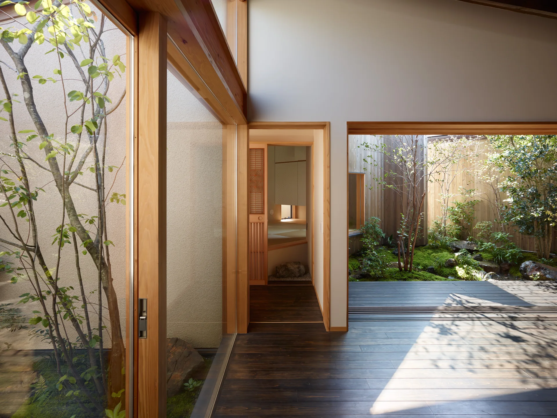 A modern Japanese interior featuring dark wood flooring, light timber frames, and a glass-enclosed central courtyard filled with moss and trees.