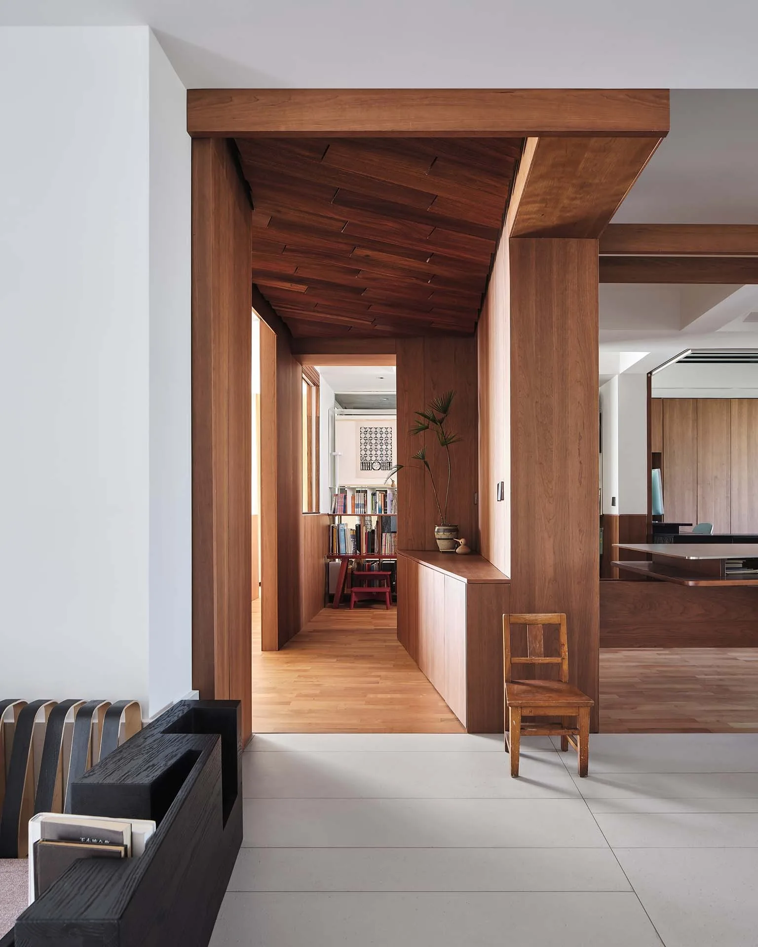 A modern interior hallway featuring rich wood paneled walls, a matching wood ceiling, integrated low cabinetry, and light floor tiling.