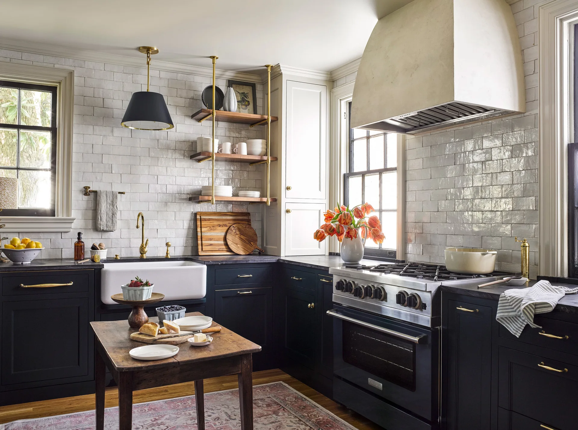 A kitchen featuring navy blue lower cabinets, a glossy white subway tile wall, a white farmhouse sink, and a large plaster range hood.