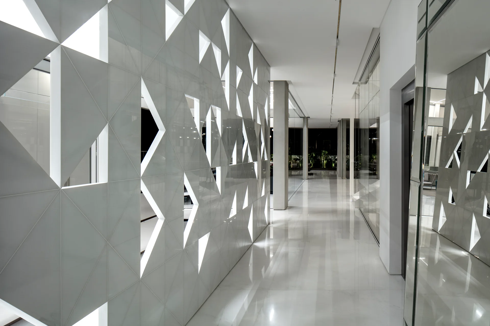 A modern hallway featuring a geometric patterned white wall with integrated lighting and a highly reflective polished floor.