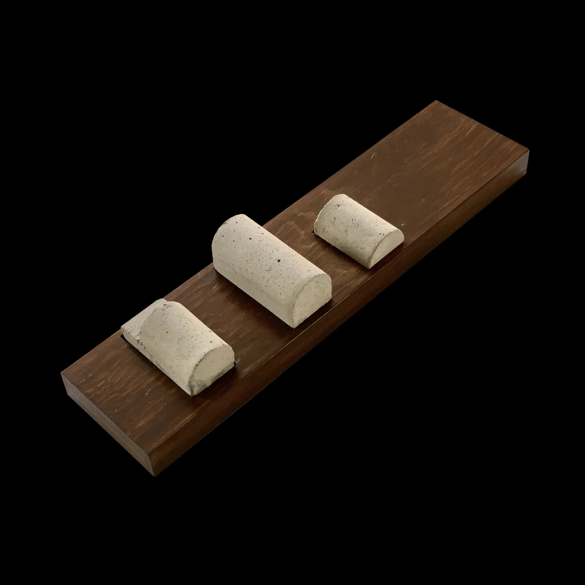 Three semicircular light grey concrete material samples arranged in a row on a long rectangular dark brown wood base against a black background.