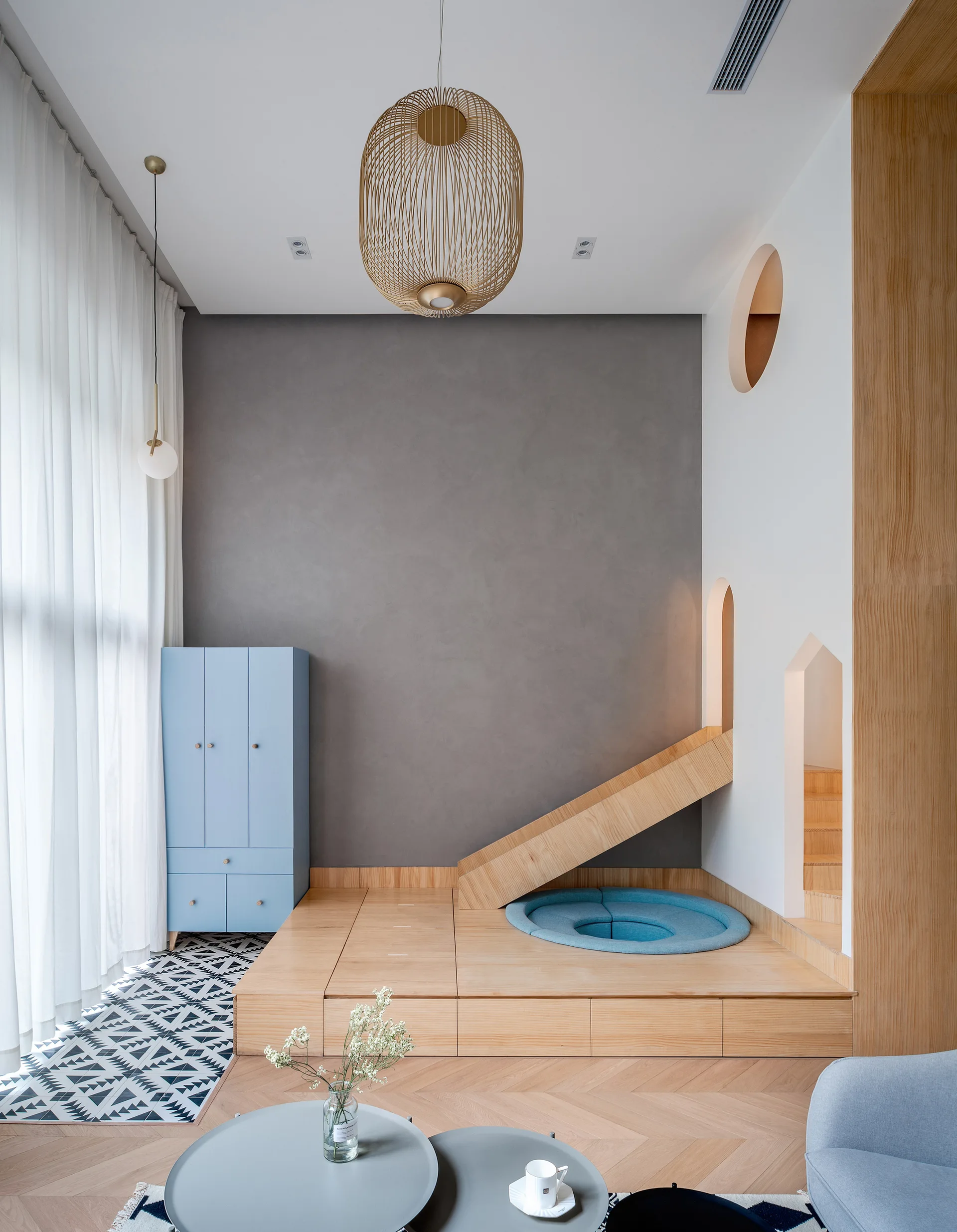 A modern children's playroom featuring a raised wooden platform with an integrated slide, a light blue storage cabinet, and a grey accent wall.