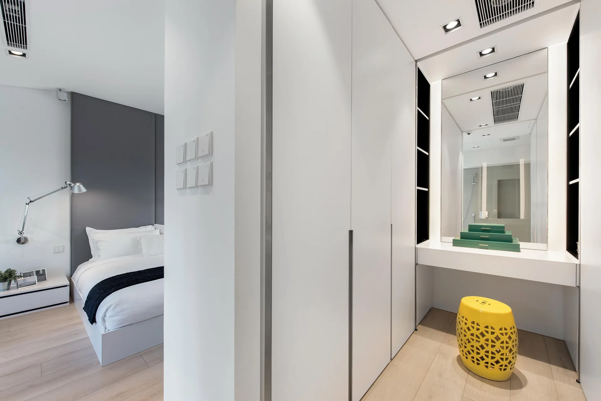 A modern dressing area with built-in white wardrobes, an integrated vanity desk, a large mirror, and a bright yellow lattice ceramic stool.