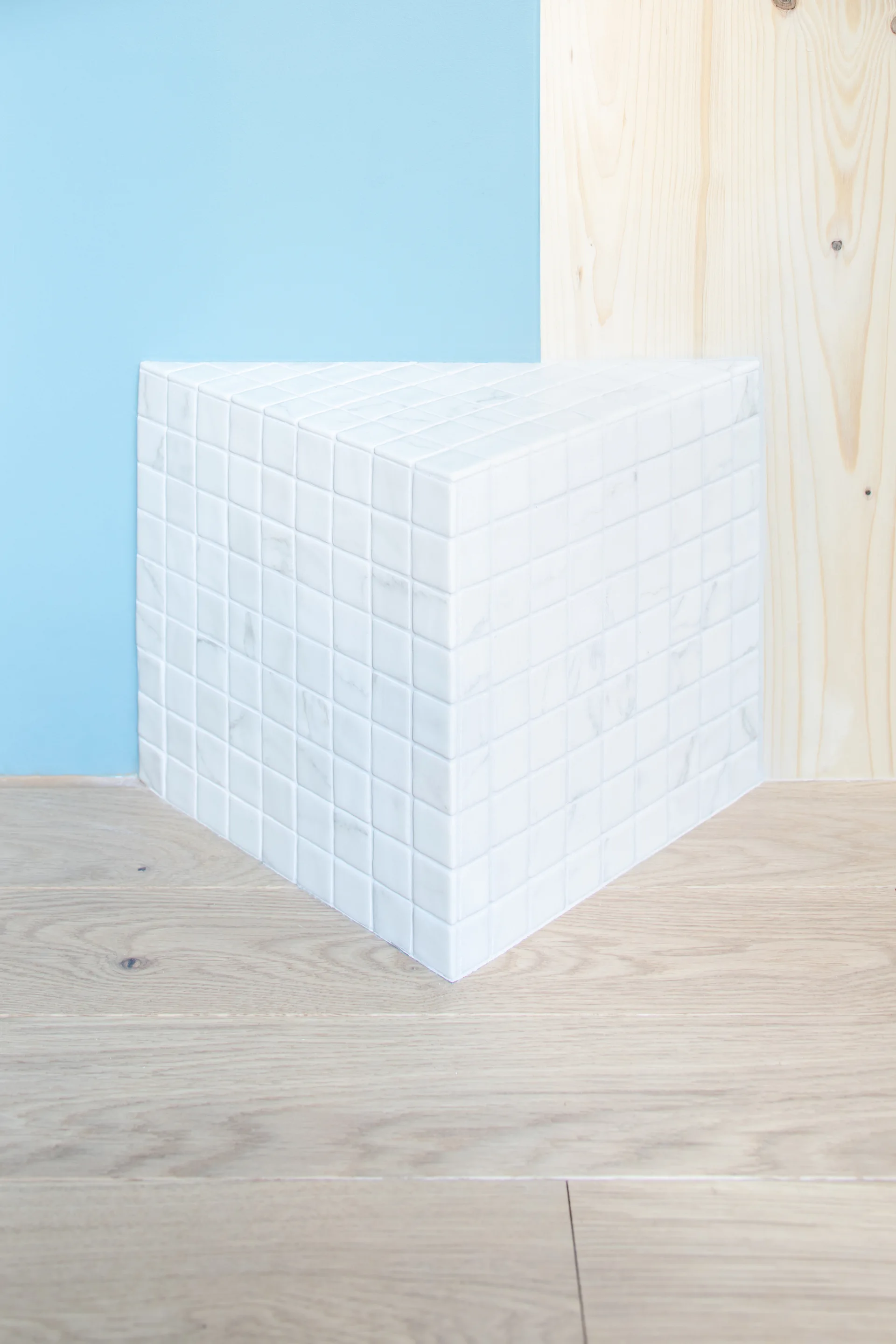 A white marble mosaic tiled corner structure stands on light wood floors before a divided blue and natural wood paneled wall.