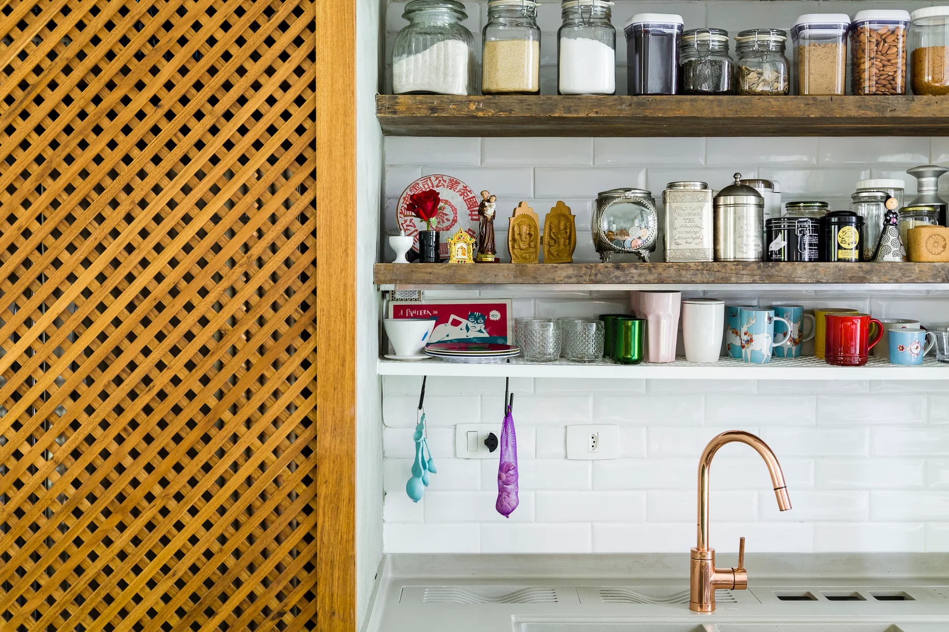 A copper faucet stands against a white subway tiled wall with rustic wood open shelves and a diagonal wood lattice partition screen on the left.