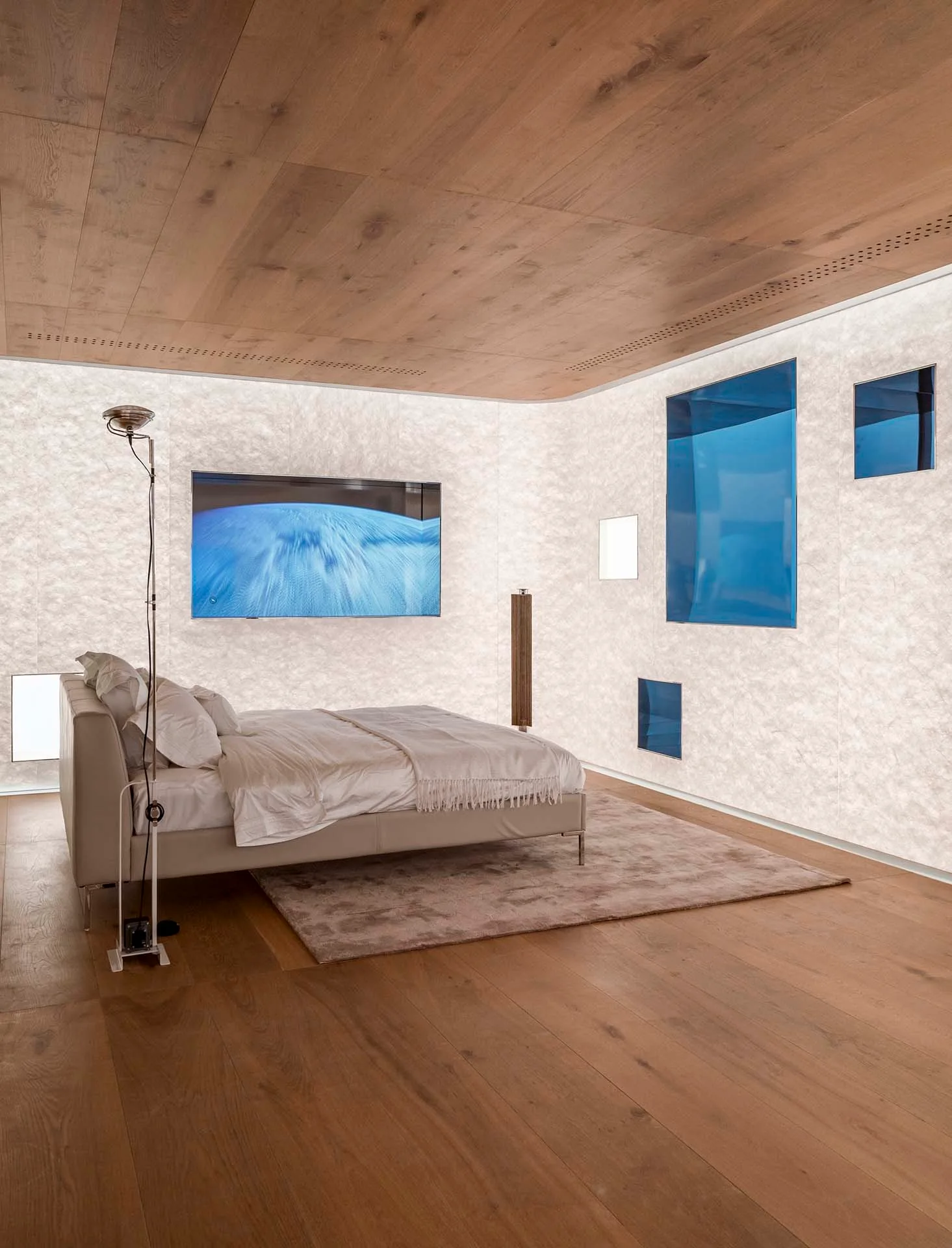 A minimalist bedroom features matching wood planks on the floor and ceiling alongside large glowing backlit wall panels and blue glass window insets.