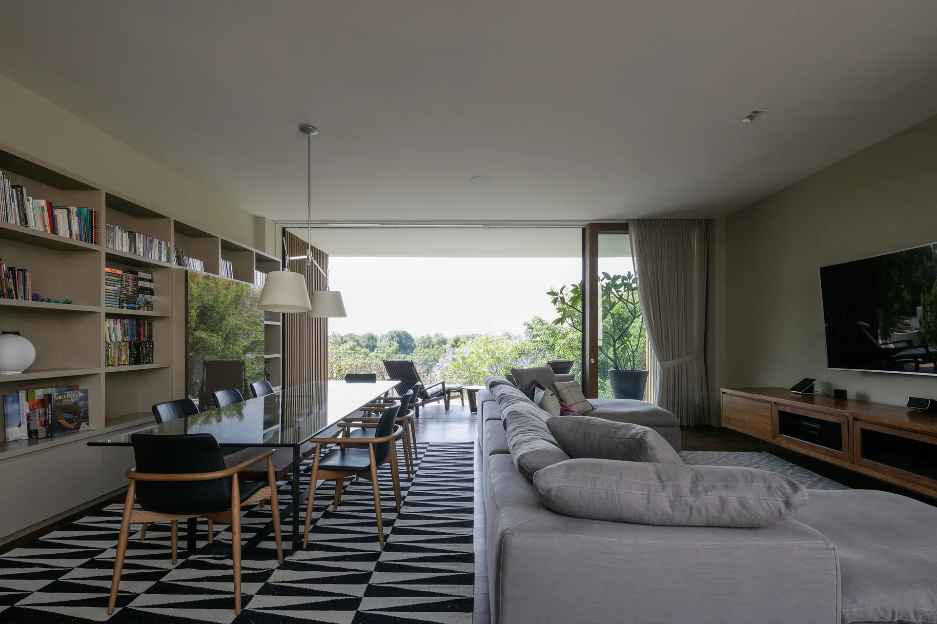 An open-plan living and dining room features a gray sectional sofa, a glass-top dining table over a geometric rug, and a terrace view.