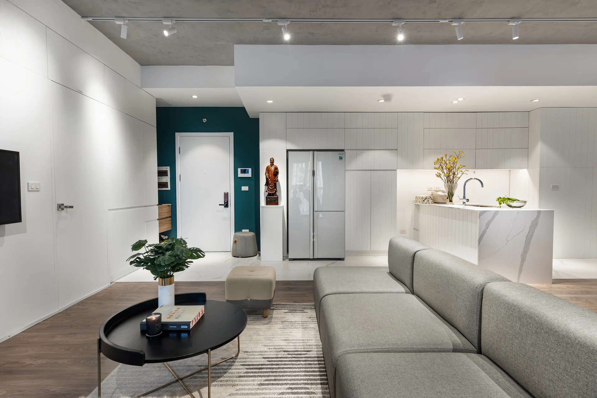 An open-concept living room features a gray sectional sofa, a black coffee table, a marble kitchen island, and a contrasting teal accent wall.