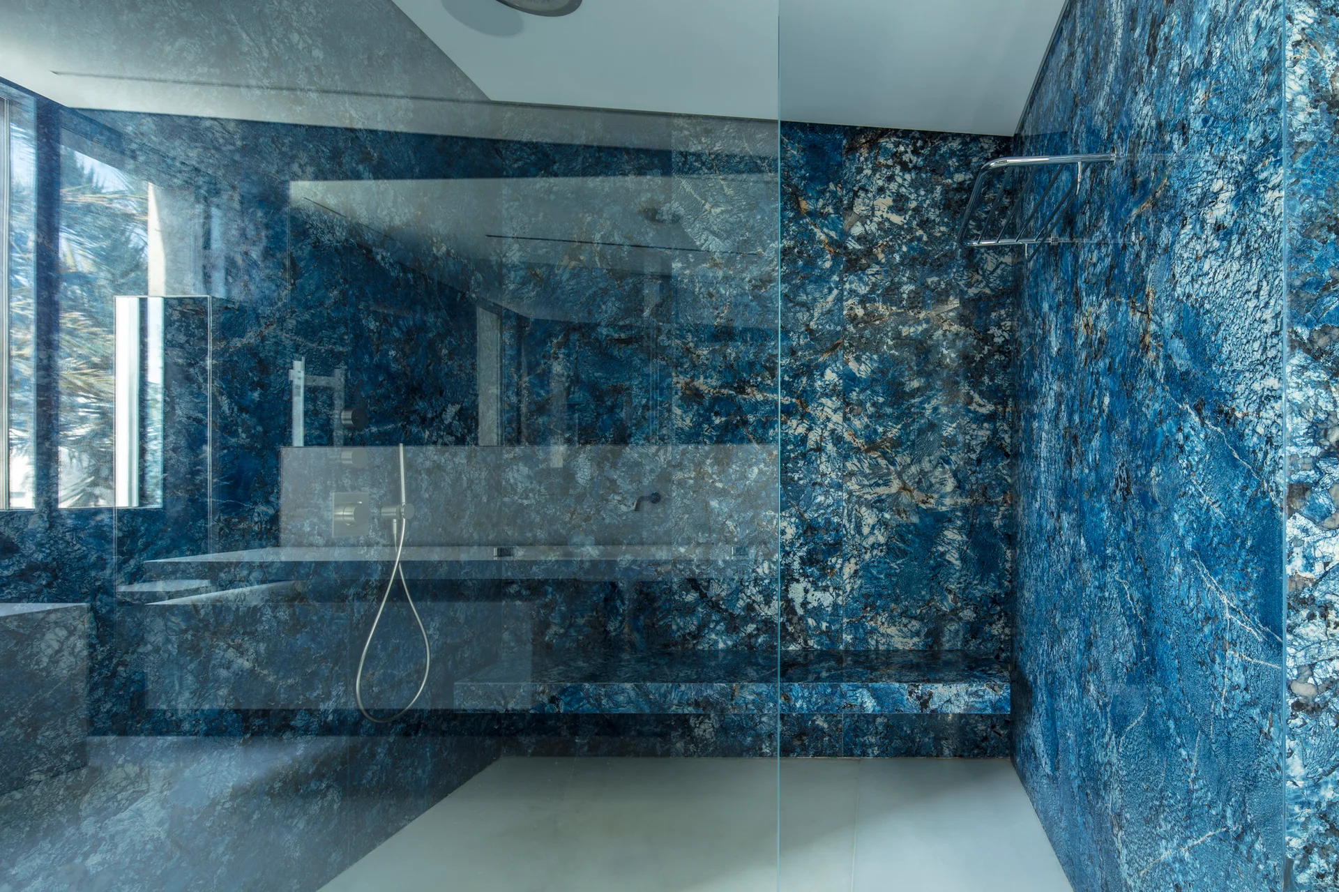 A modern walk-in shower features vibrant blue veined stone walls, a matching built-in stone bench, a glass partition, and metallic fixtures.