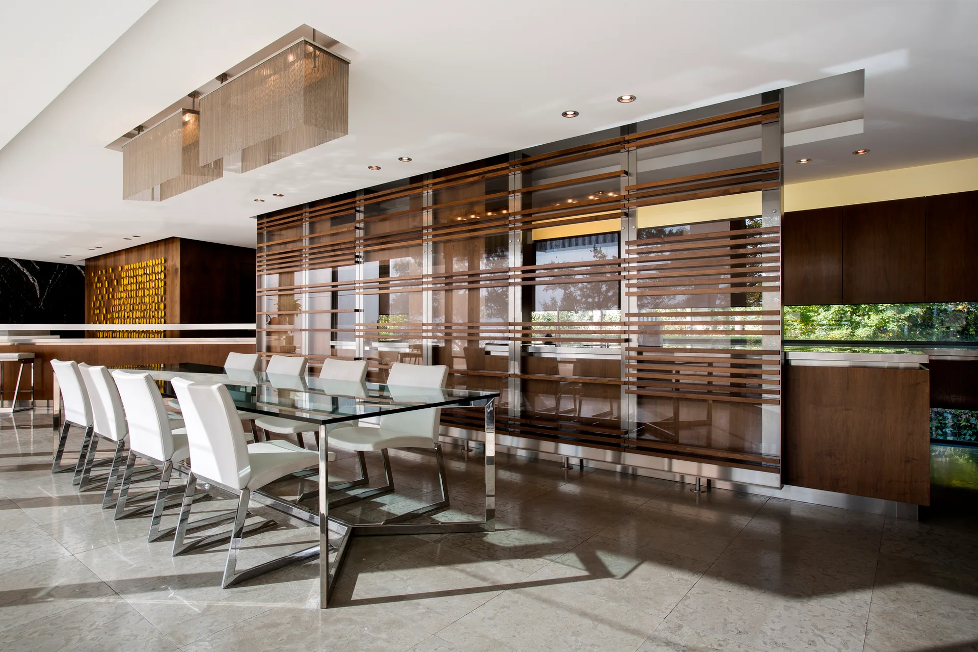 A modern dining room featuring a rectangular glass table, white chairs, and a large wood slatted wall partition next to polished floor tiles.
