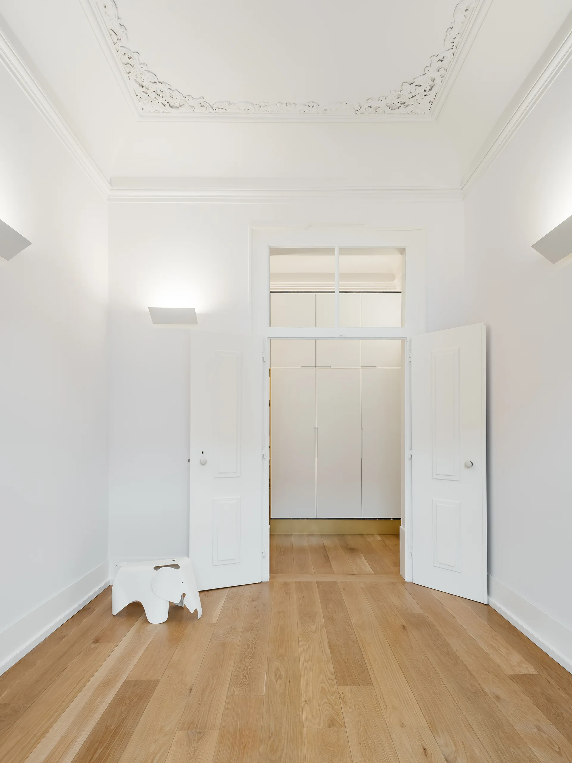 A bright entryway features light wood floors, tall white double doors with a transom window, and an ornate plaster ceiling medallion.