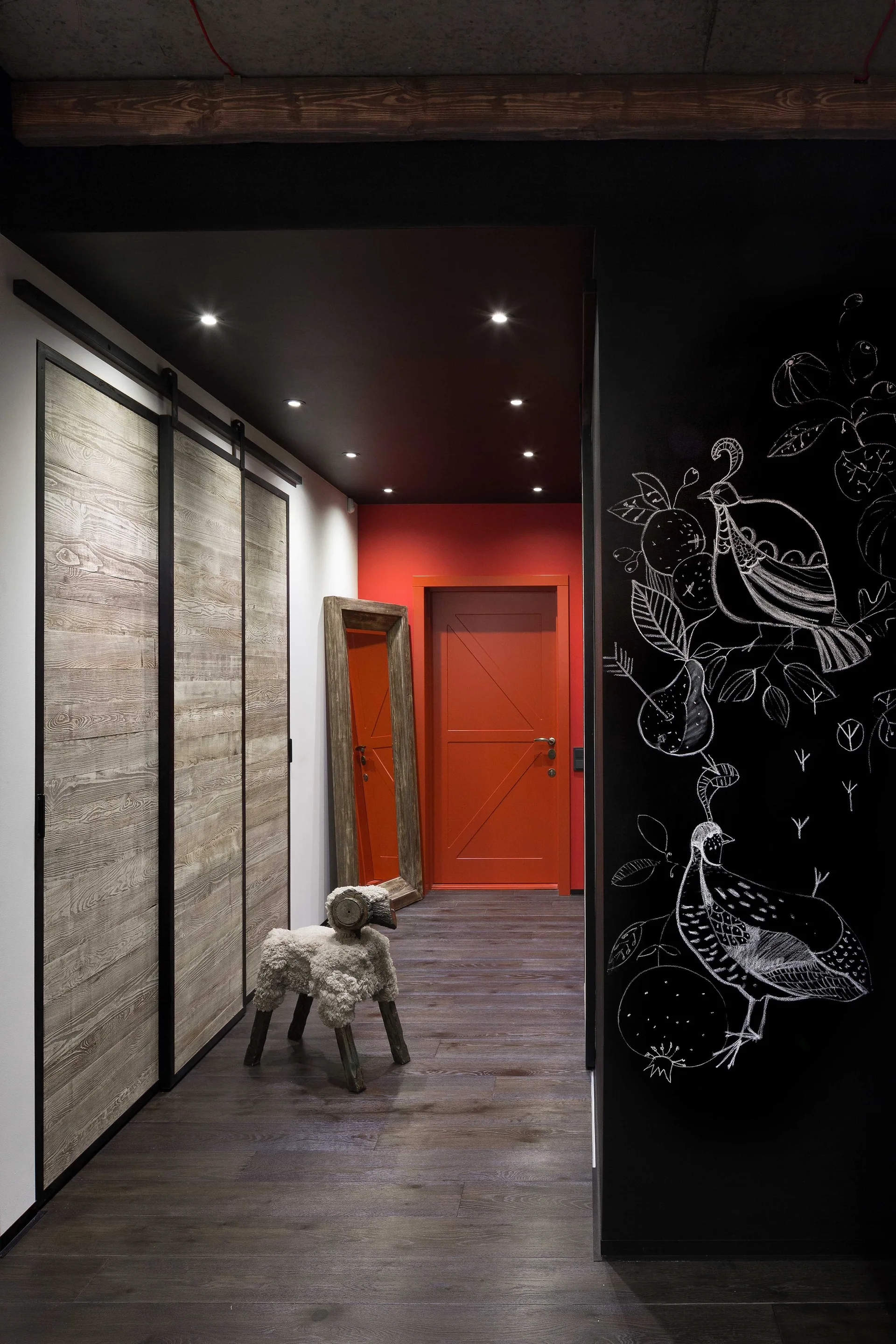 A moody hallway featuring rustic wood sliding doors, a black chalkboard wall with chalk drawings, and a bright red door at the far end.