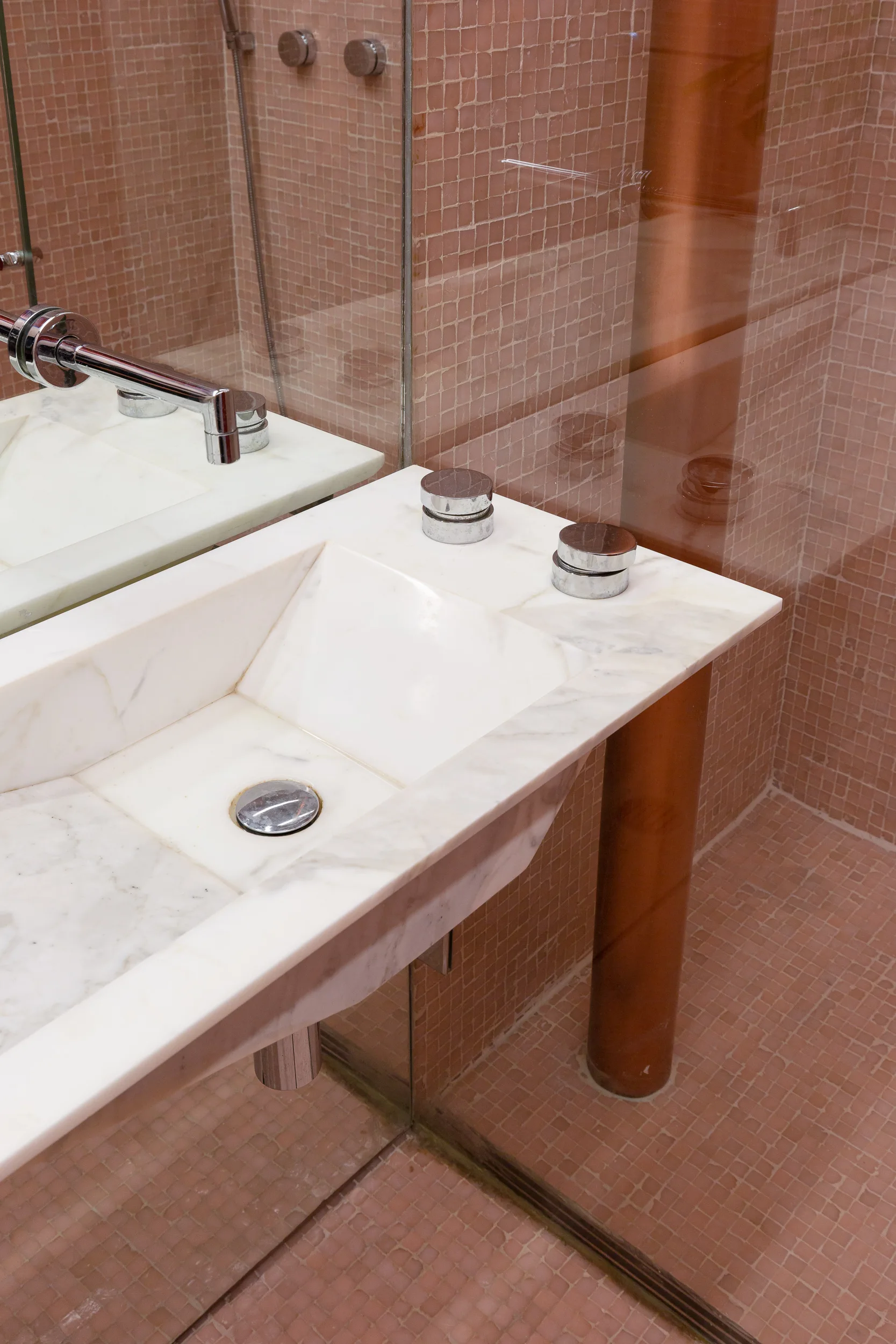A white marble vanity with an integrated basin and chrome fixtures sits against pink mosaic tiled walls in a modern bathroom.