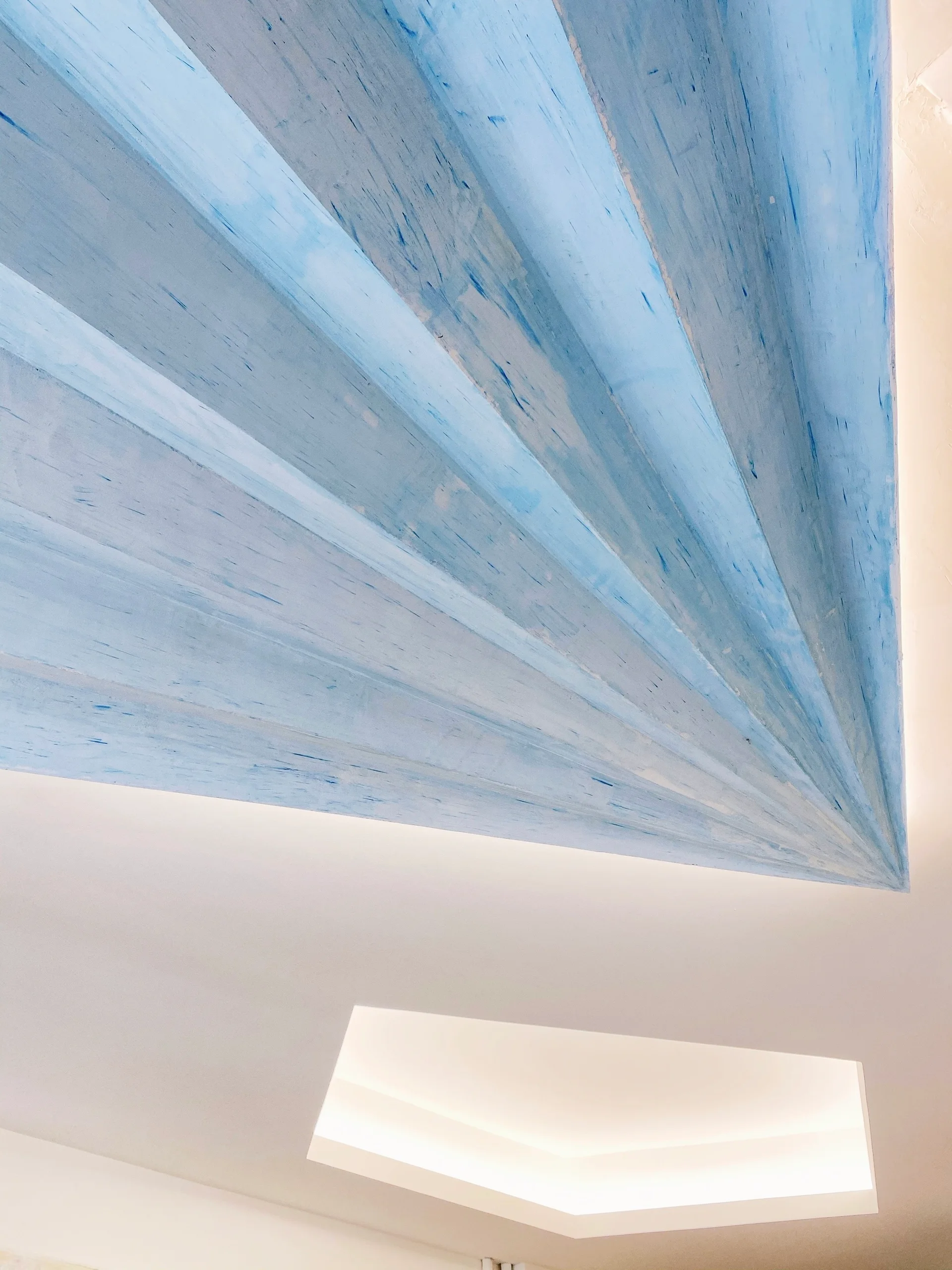 An angular architectural ceiling featuring textured blue painted panels next to a white recessed lighting fixture.
