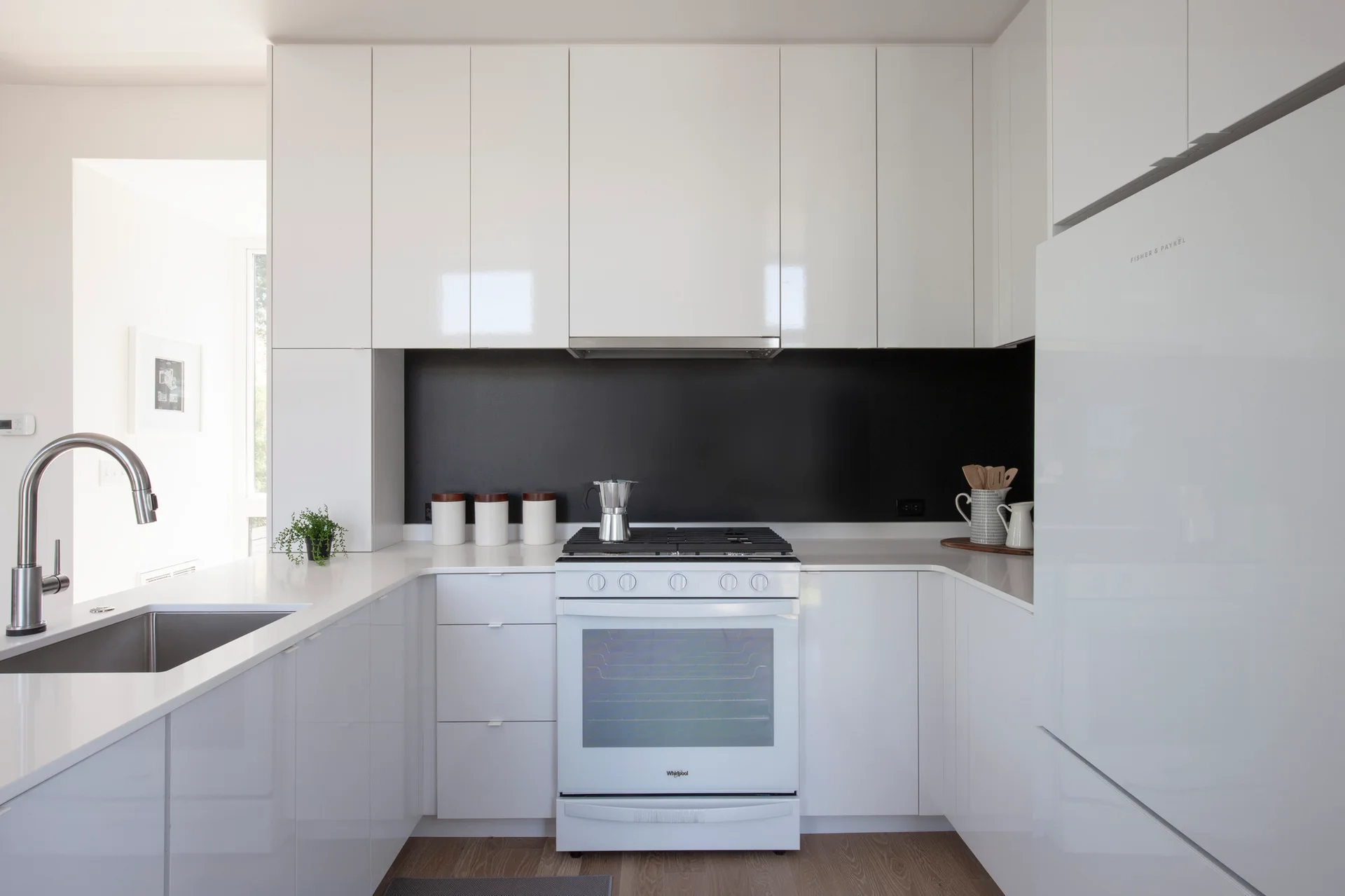A contemporary U-shaped kitchen features high-gloss white cabinets, a solid black backsplash, and a white stove.