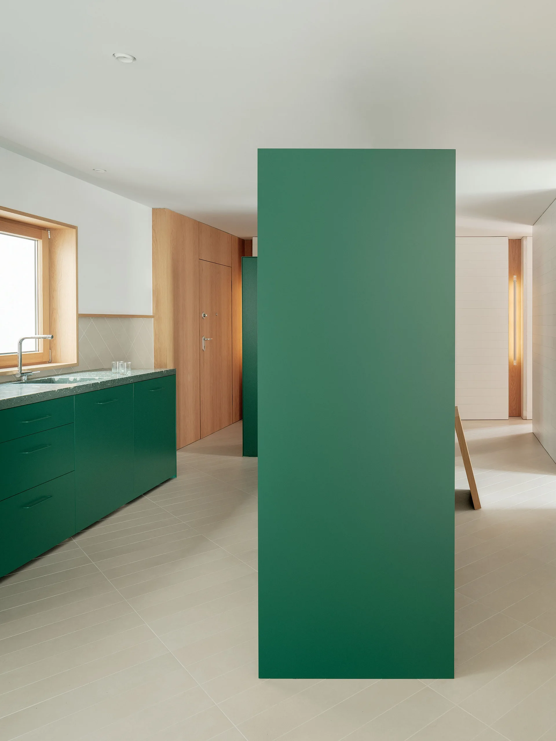 A minimalist kitchen featuring matte forest green cabinets, a matching vertical partition, and light wood wall panels.