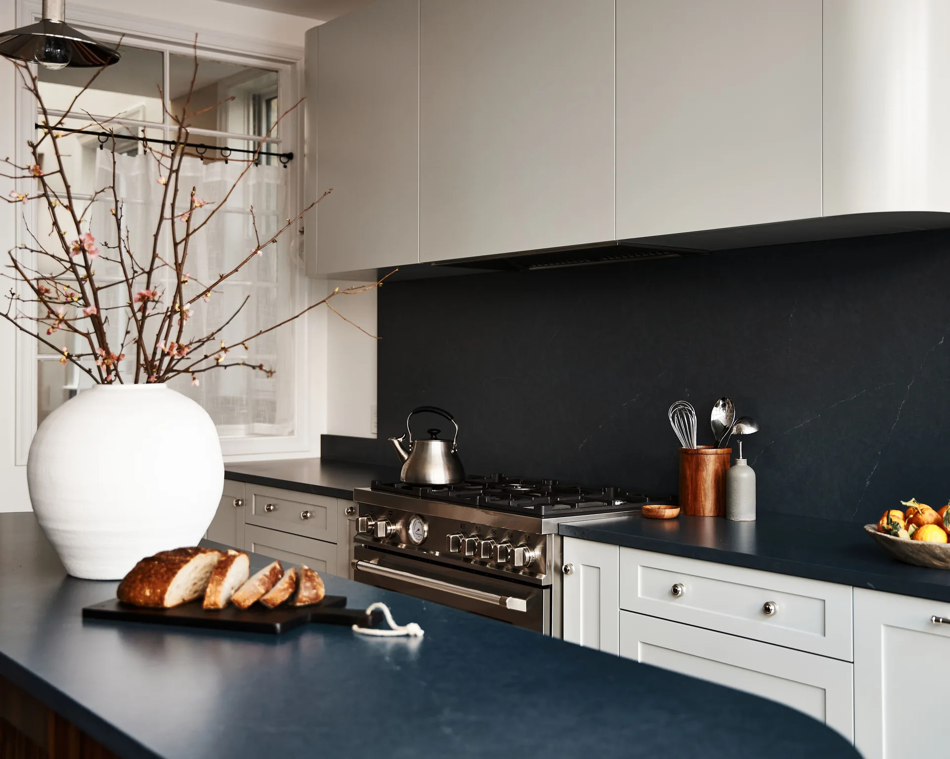 A kitchen featuring light gray upper cabinets, white shaker lower cabinets, dark blue countertops, and a professional stainless steel range.