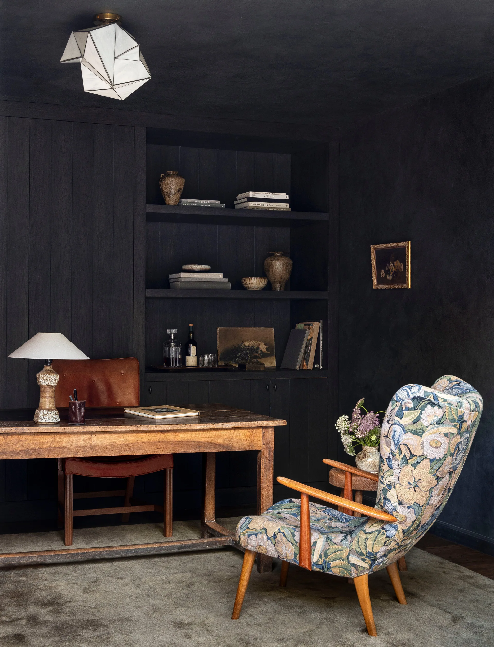 A dark charcoal study features a rustic wooden desk, a brown leather chair, and an armchair upholstered in a floral pattern.