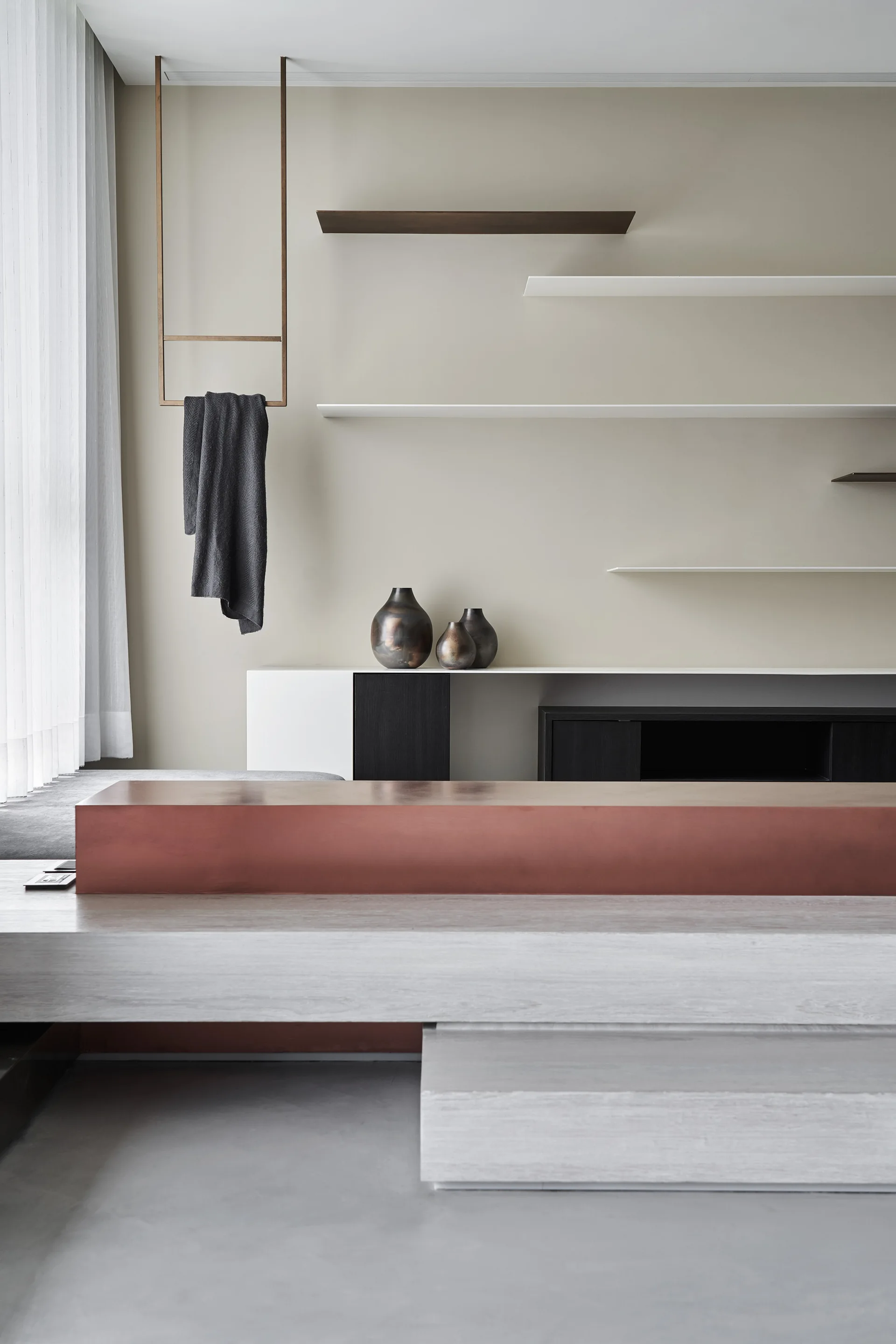 A minimalist living room features a stepped platform bench, asymmetrical floating shelves on a beige wall, and a low console table.