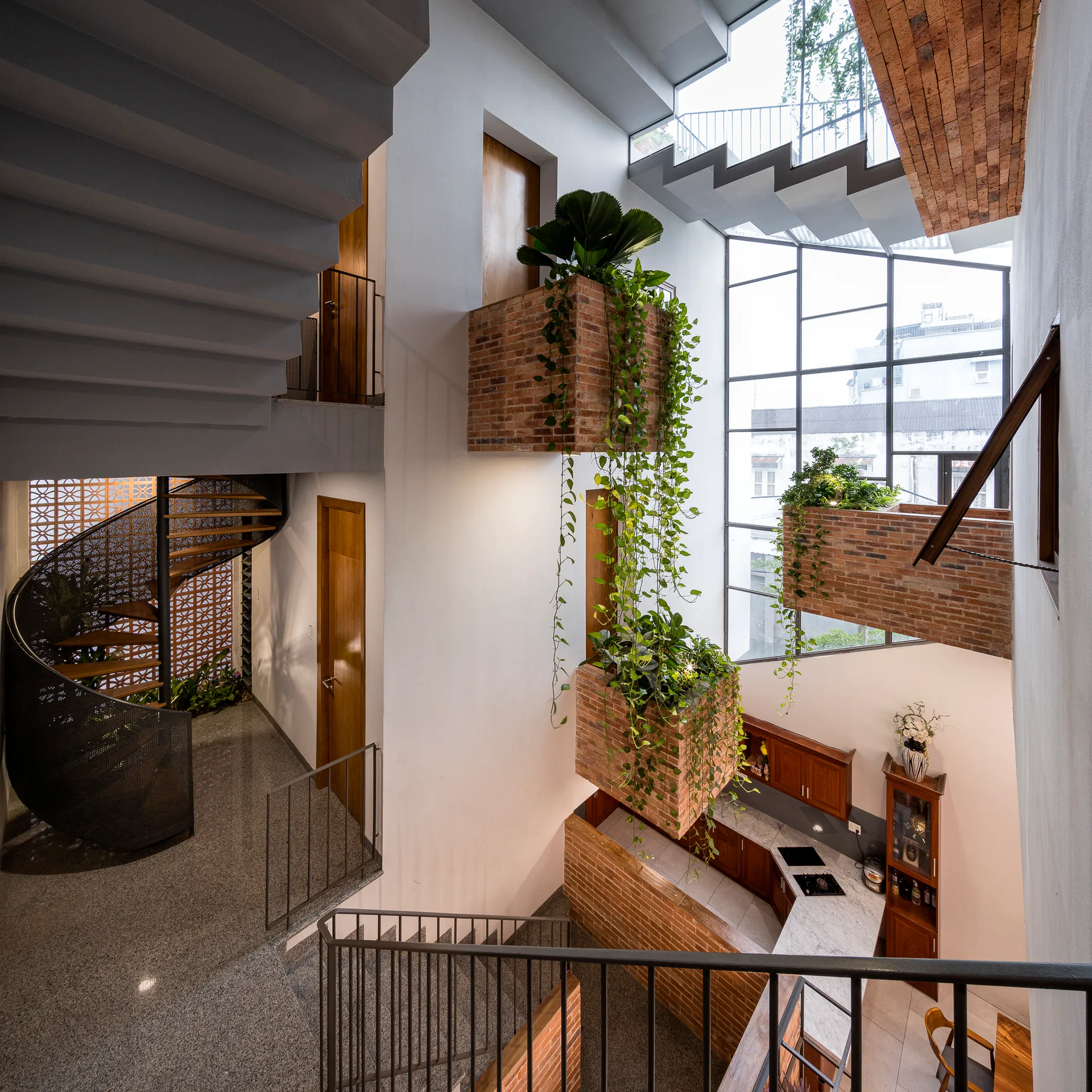 A multi-level interior atrium features suspended brick planter boxes with cascading vines, a metal staircase, and a large multi-pane window.