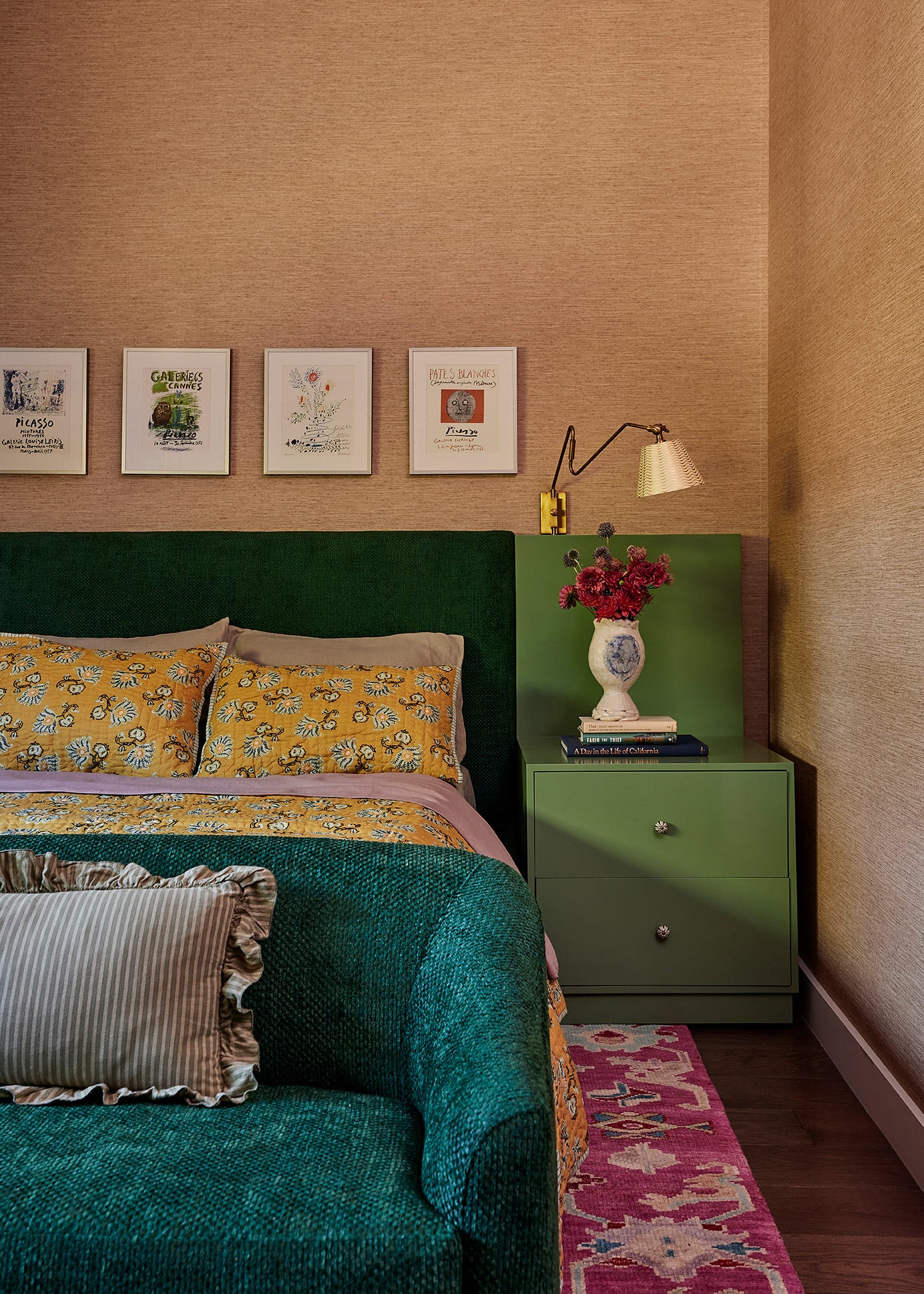 A bedroom vignette features a green upholstered headboard, a matching green nightstand, textured tan wallpaper, and a row of four small framed prints.