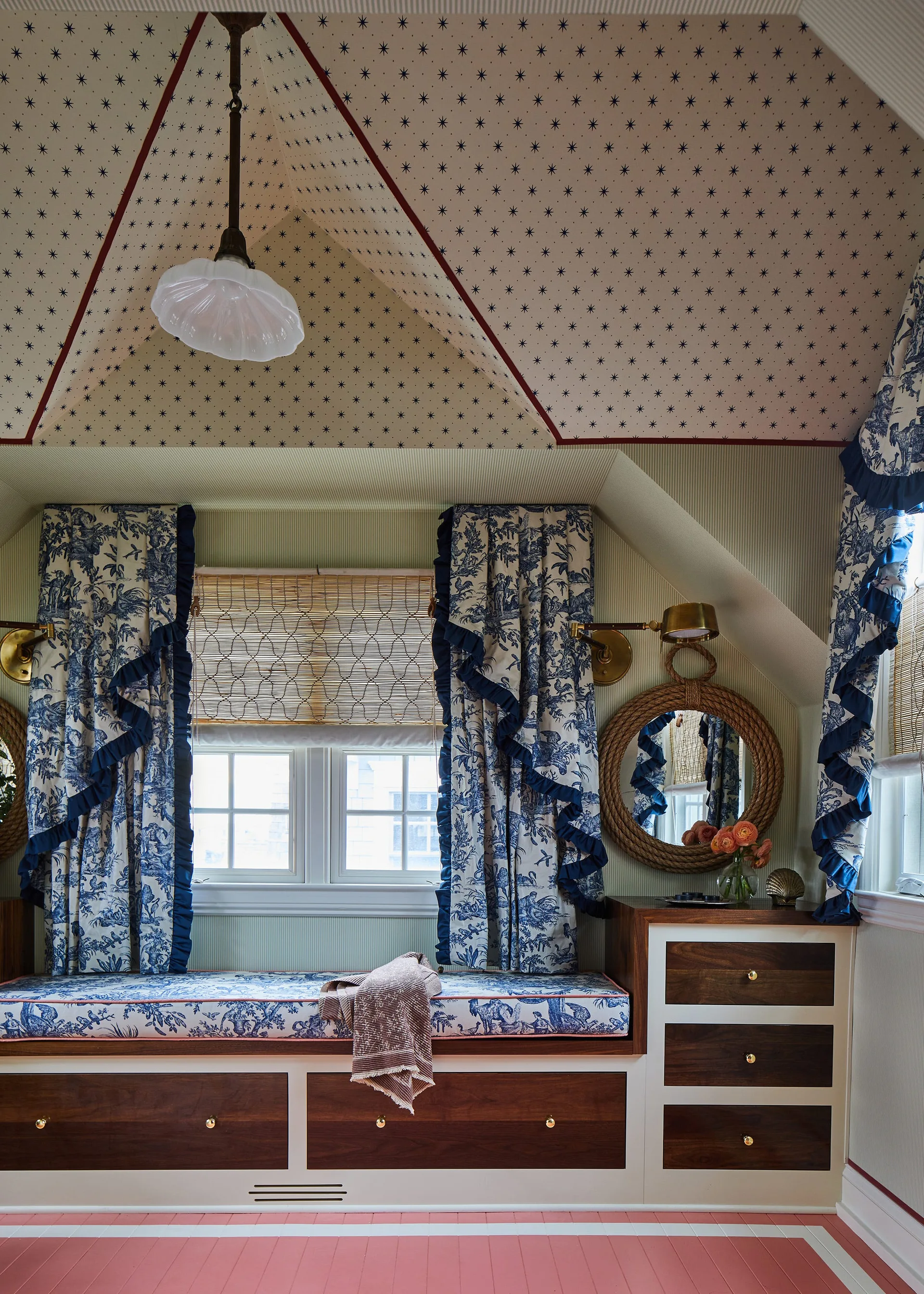 A built-in window seat in a dormer bedroom features blue and white toile cushions, a starry wallpapered ceiling, and dark wood drawers.