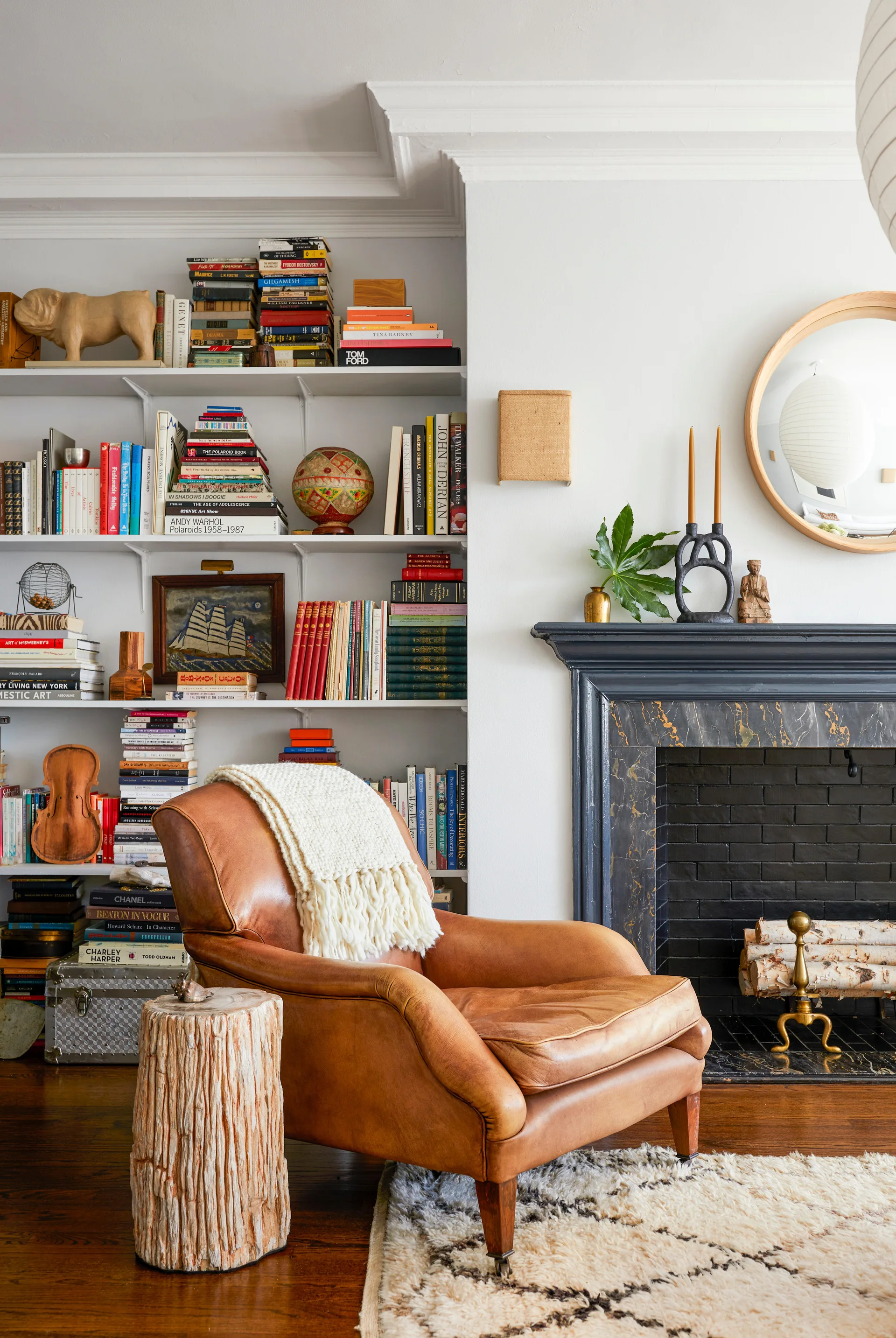 A brown leather armchair with a white knit throw sits beside a black marble fireplace and floor-to-ceiling bookshelves in a living room.