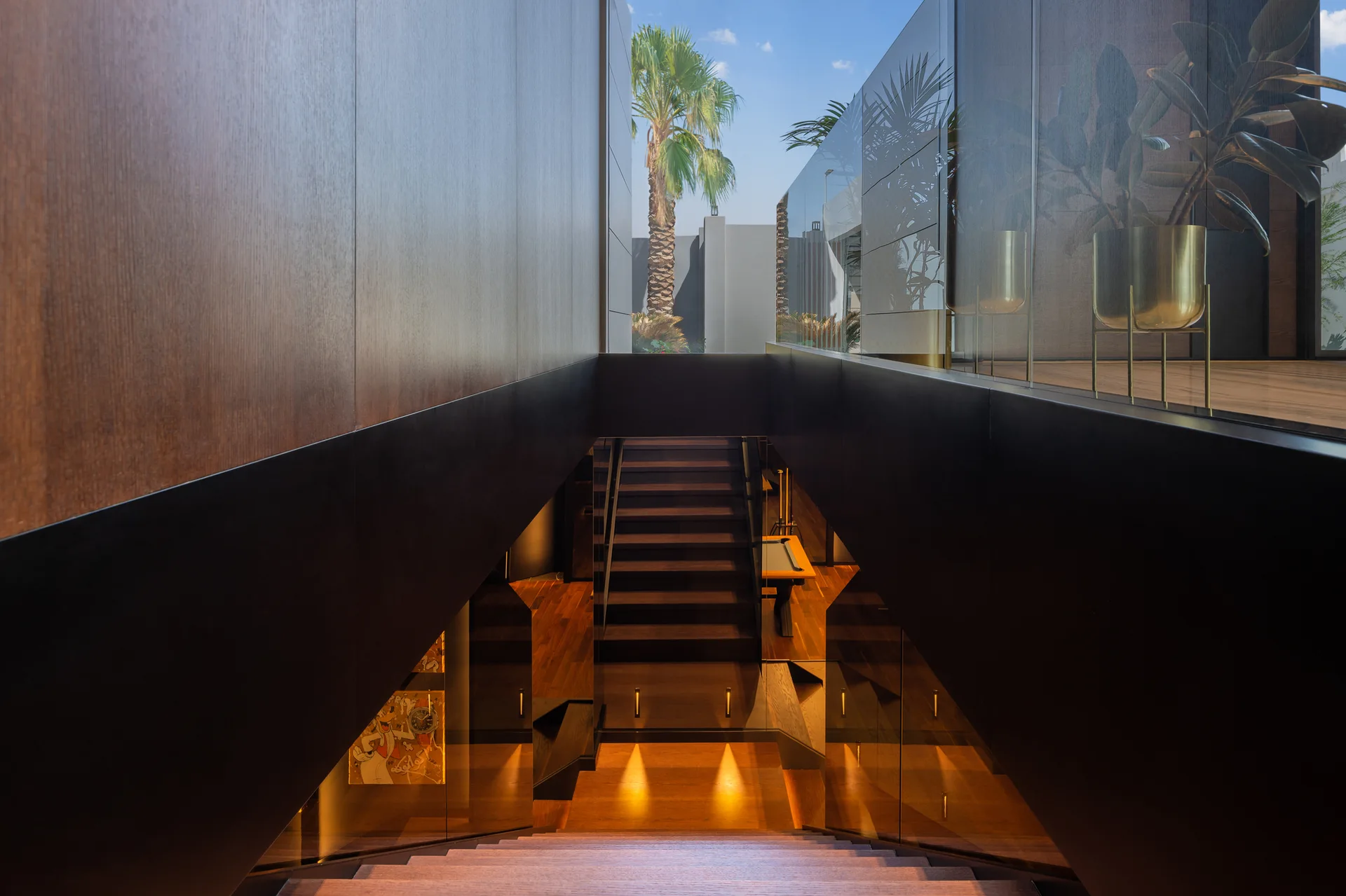 A symmetrical modern staircase with dark wood wall paneling, glass railings, and warm accent lighting on the steps.