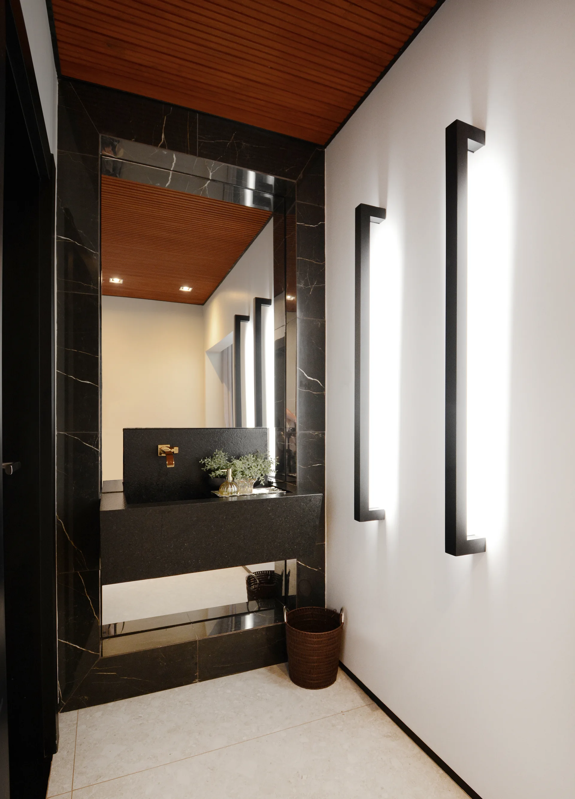 A modern powder room featuring a black stone floating vanity, a large framed mirror, vertical wall sconces, and a slatted wood ceiling.