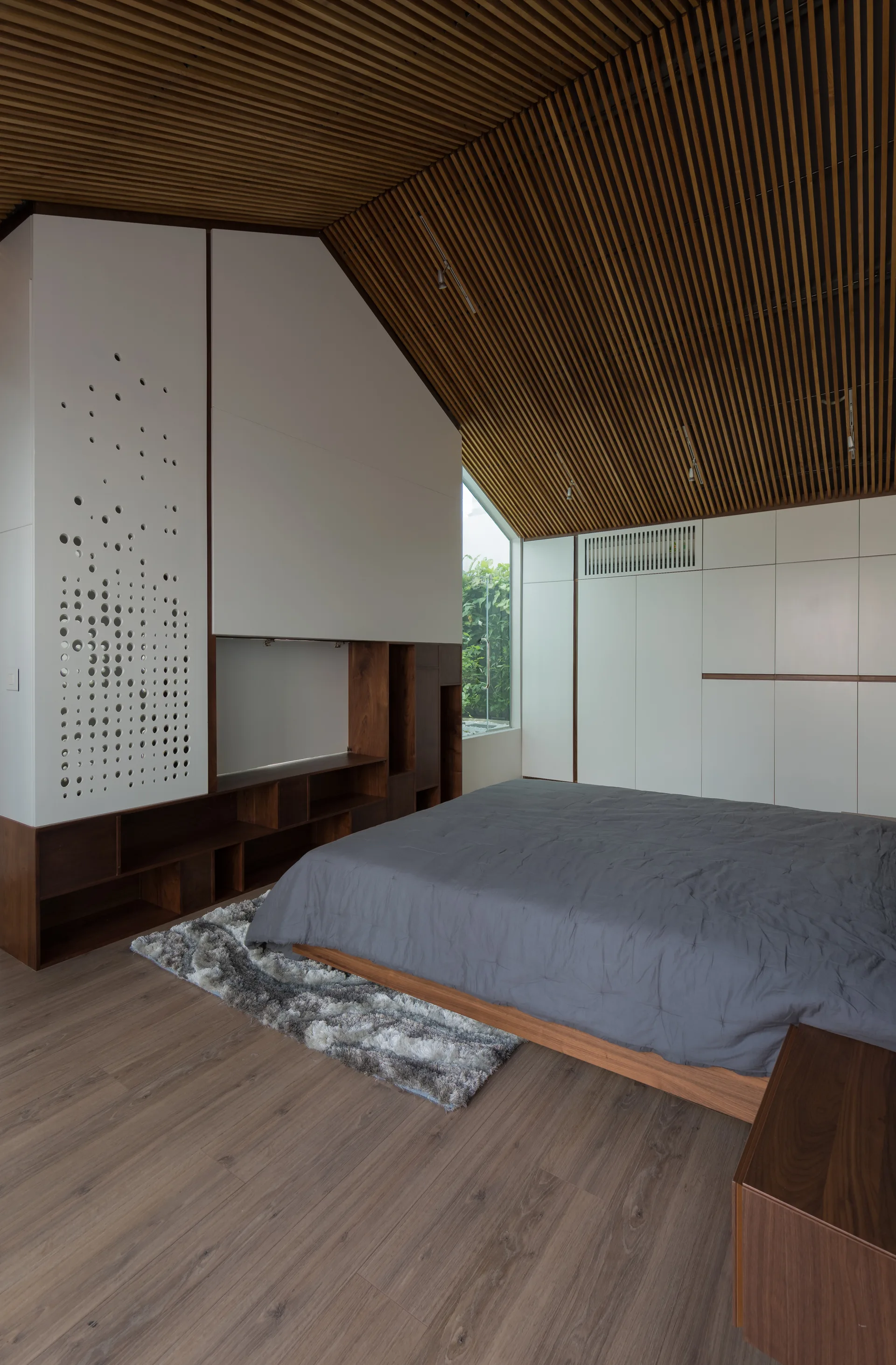 A modern bedroom featuring a slatted wood ceiling, a low-profile bed with a grey duvet, and white built-in storage cabinetry.